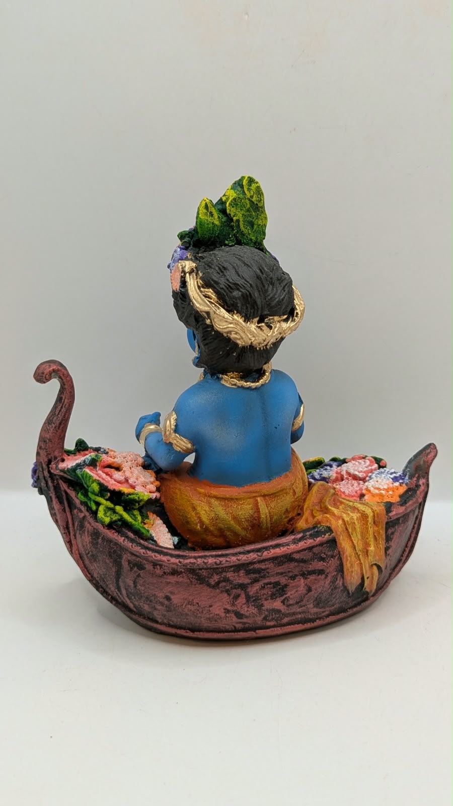 Blue baby Krishna statue on flower boat, back view