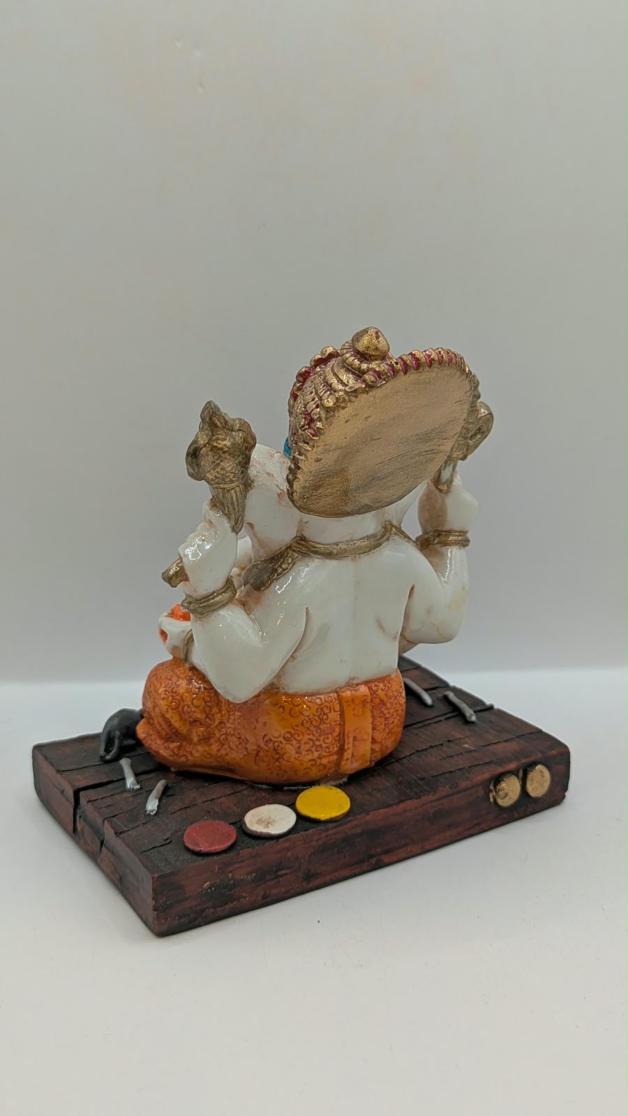 White and orange Ganesh resin statue on wood-look base, back view