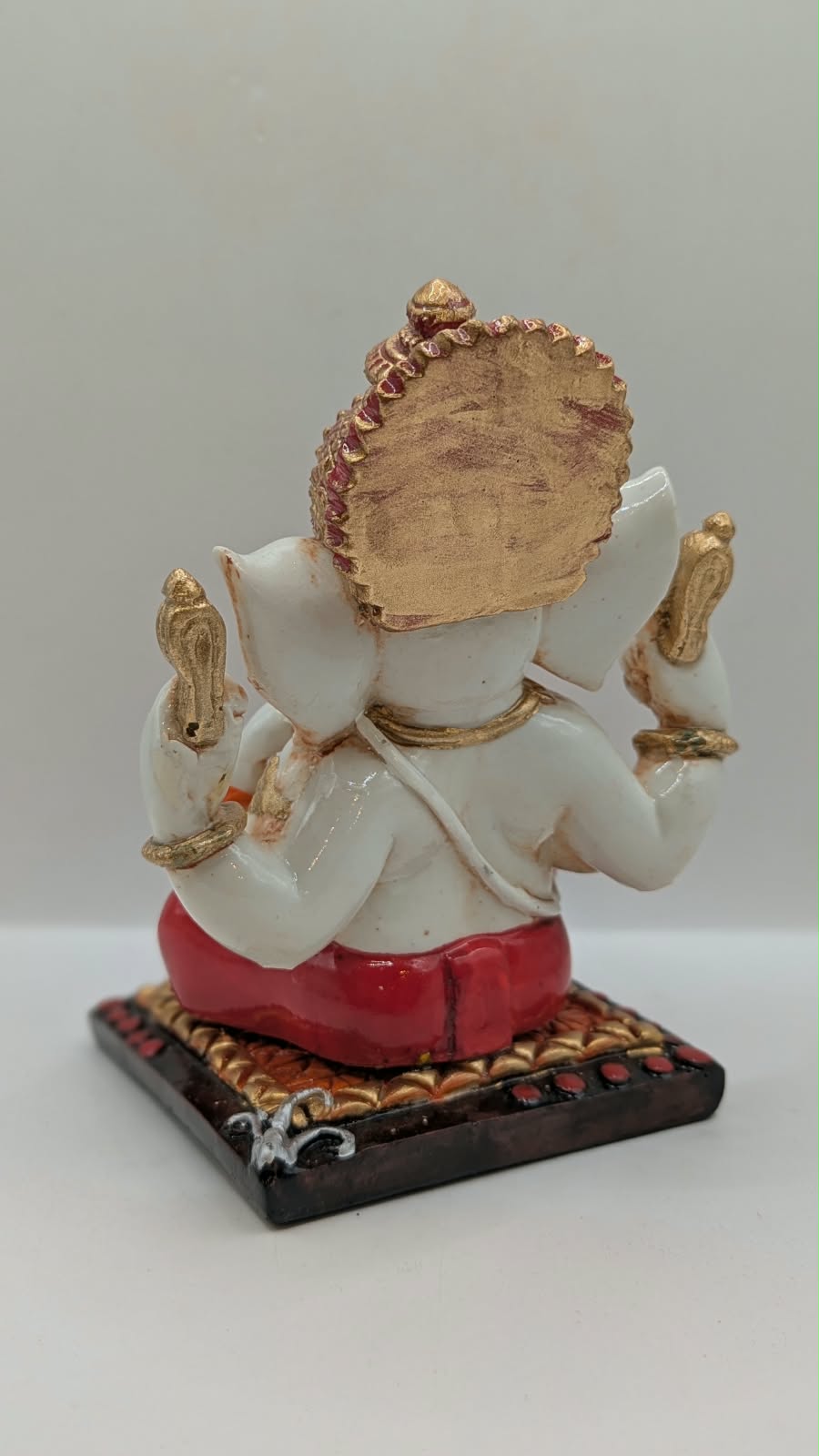 White and red Ganesh resin statue with copper crown, back view