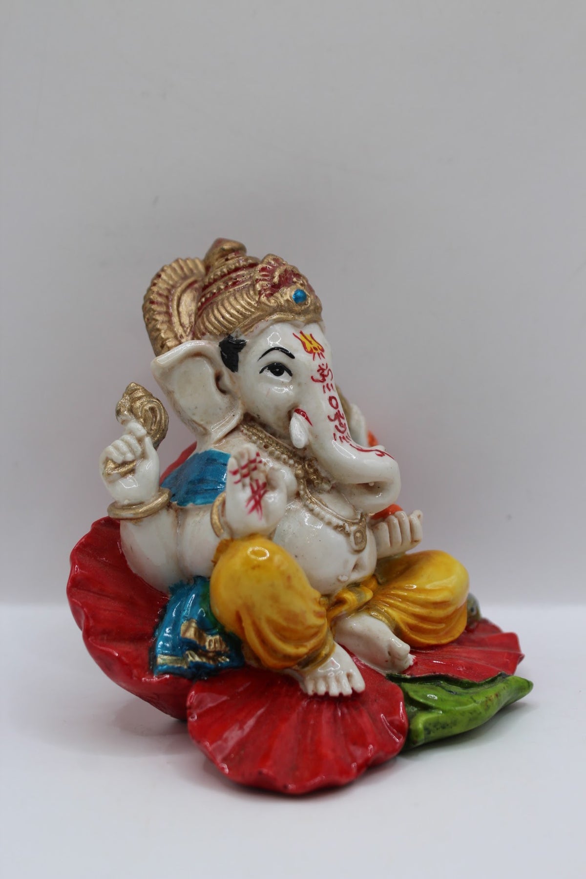 Resin Ganesh murti on red leaf, yellow dhoti, left side view