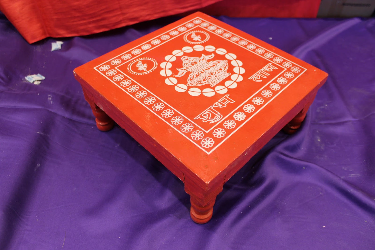 Angled view of red wooden bajot pooja chowki showing turned legs