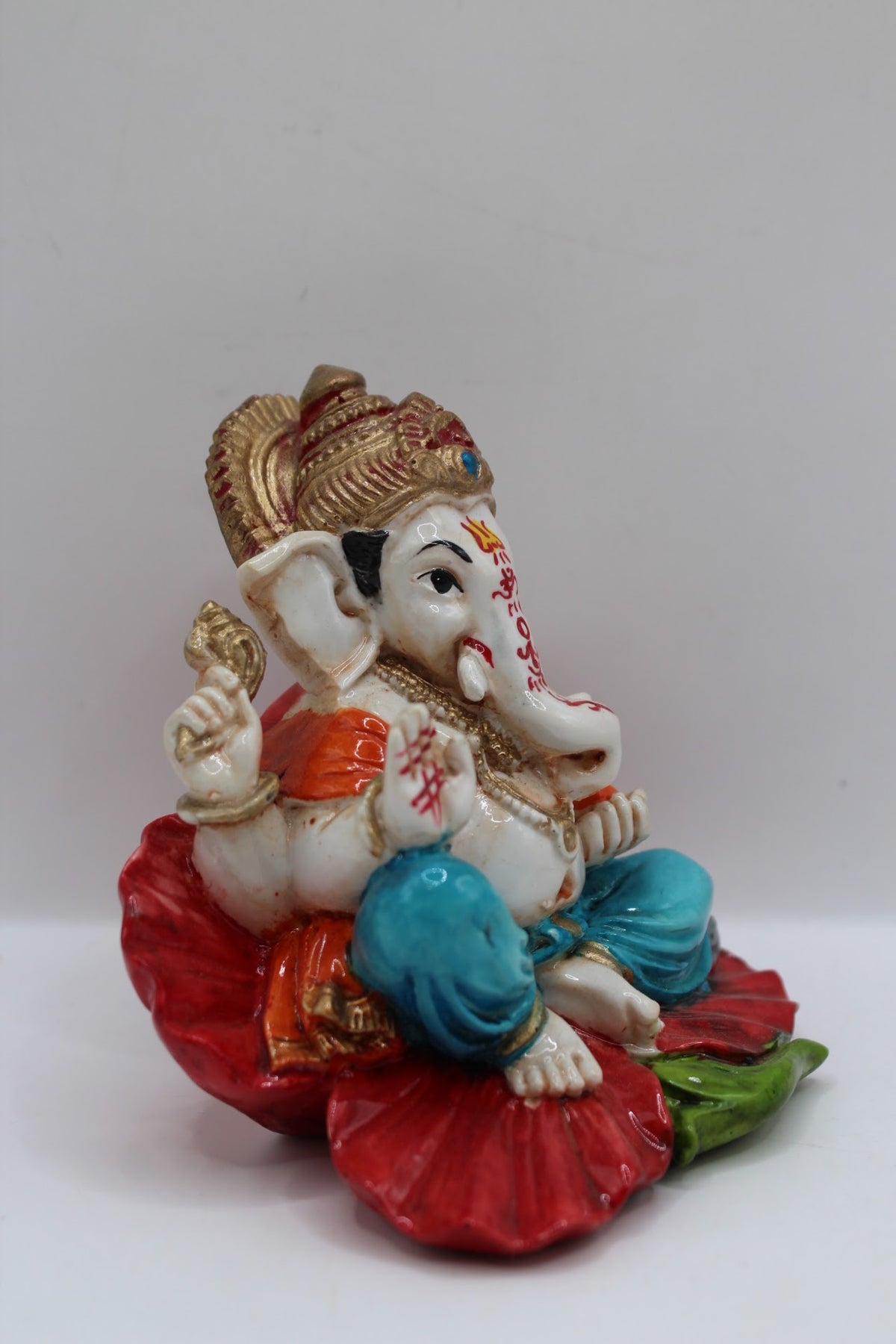 Resin Ganesh murti on red leaf, blue dhoti, left side view
