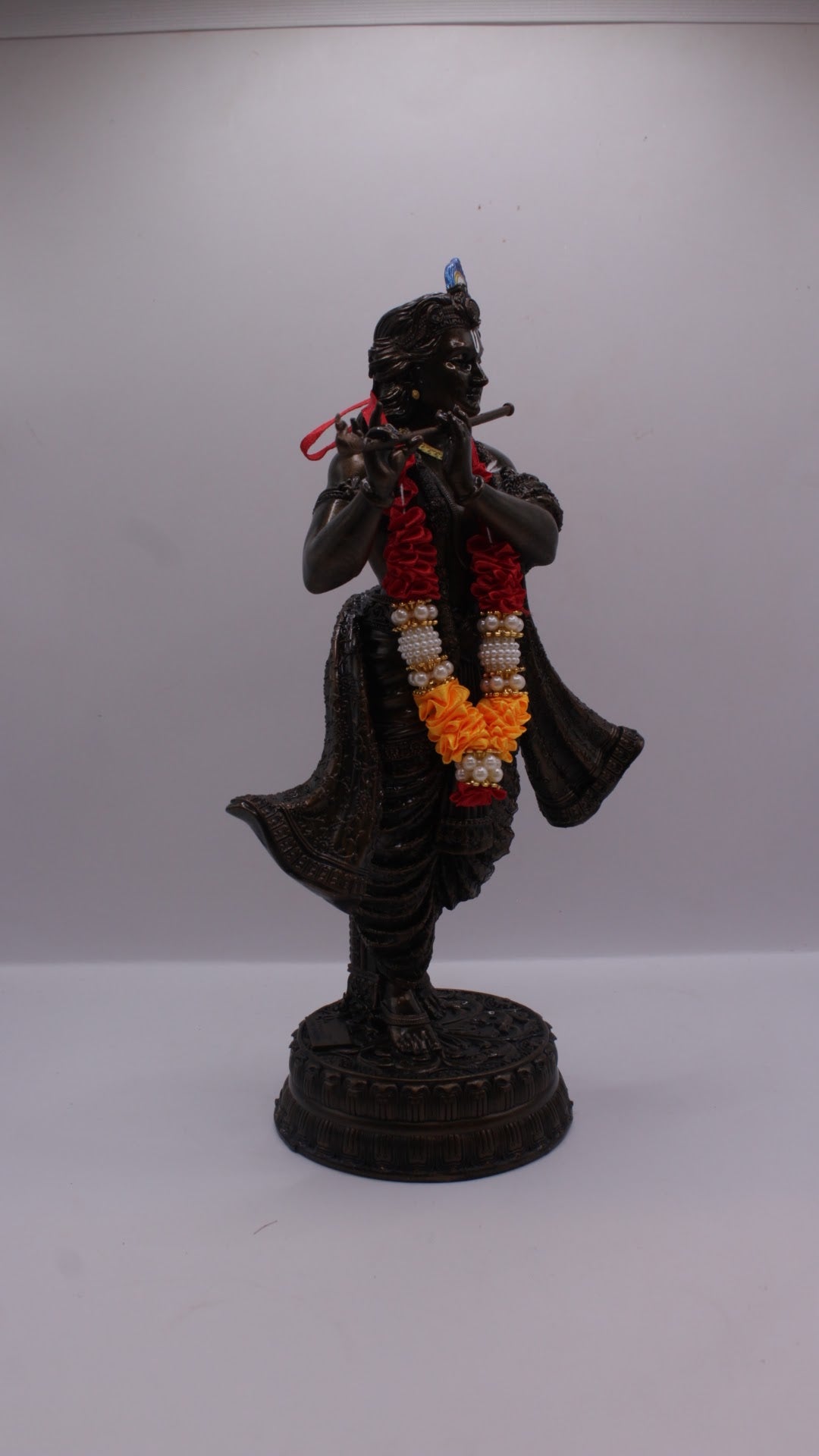 Dark finish resin Krishna statue playing flute, with garland, left side view