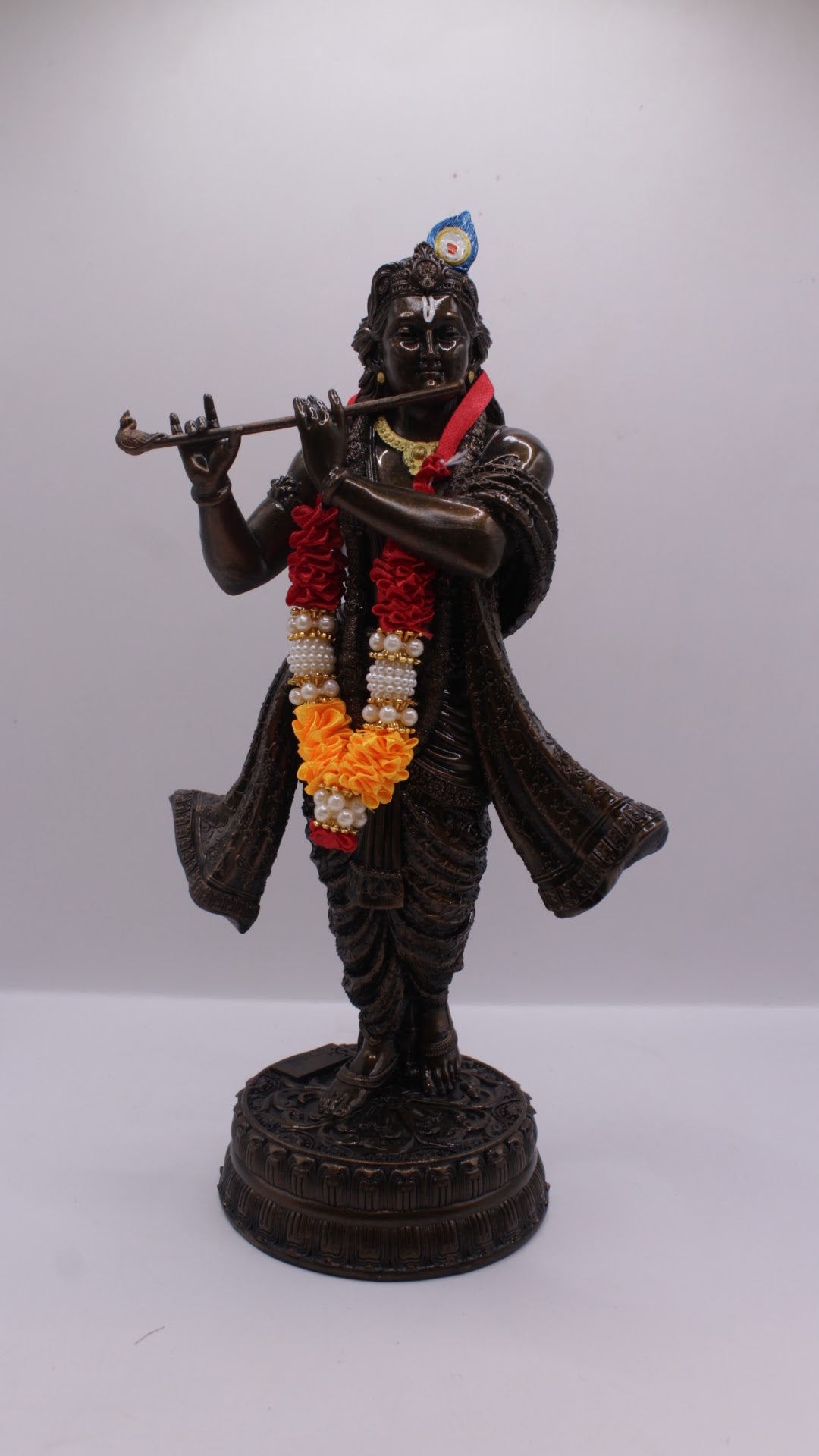 Dark finish resin Krishna statue playing flute, with garland, front view