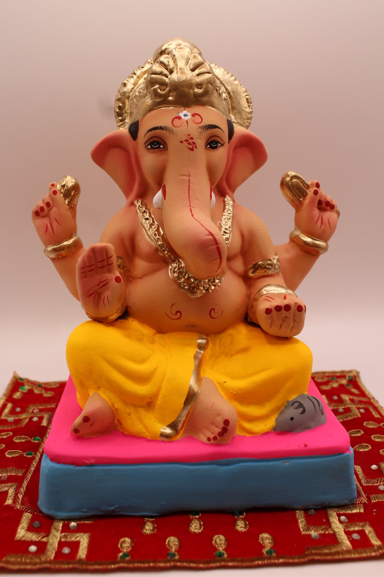 Eco-friendly 8 inch Ganesh Visarjan idol with yellow dhoti and gold fan crown on pink cushion – front view