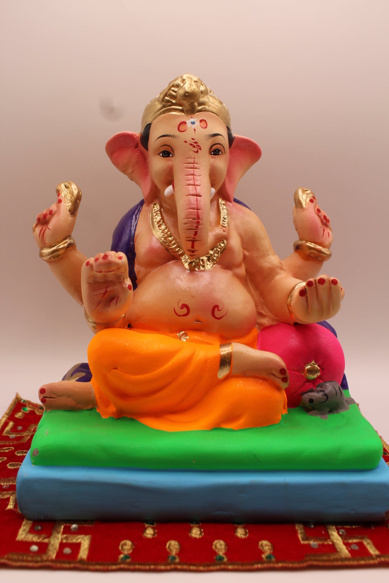 Eco-friendly 8 inch Ganesh Visarjan idol in purple shawl and orange dhoti on green mat – front view