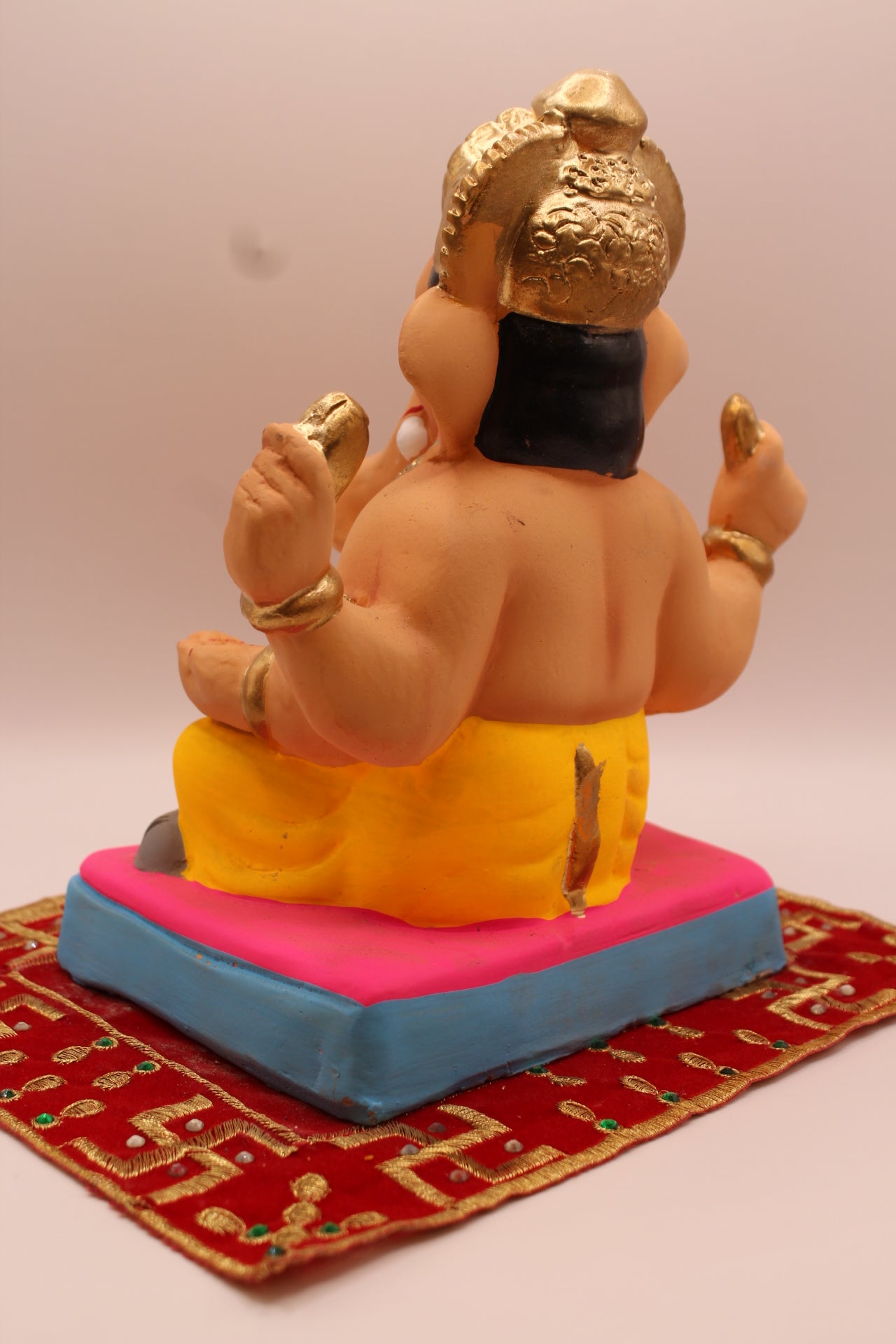 Back view – yellow dhoti and carved gold mukut on a pink mat