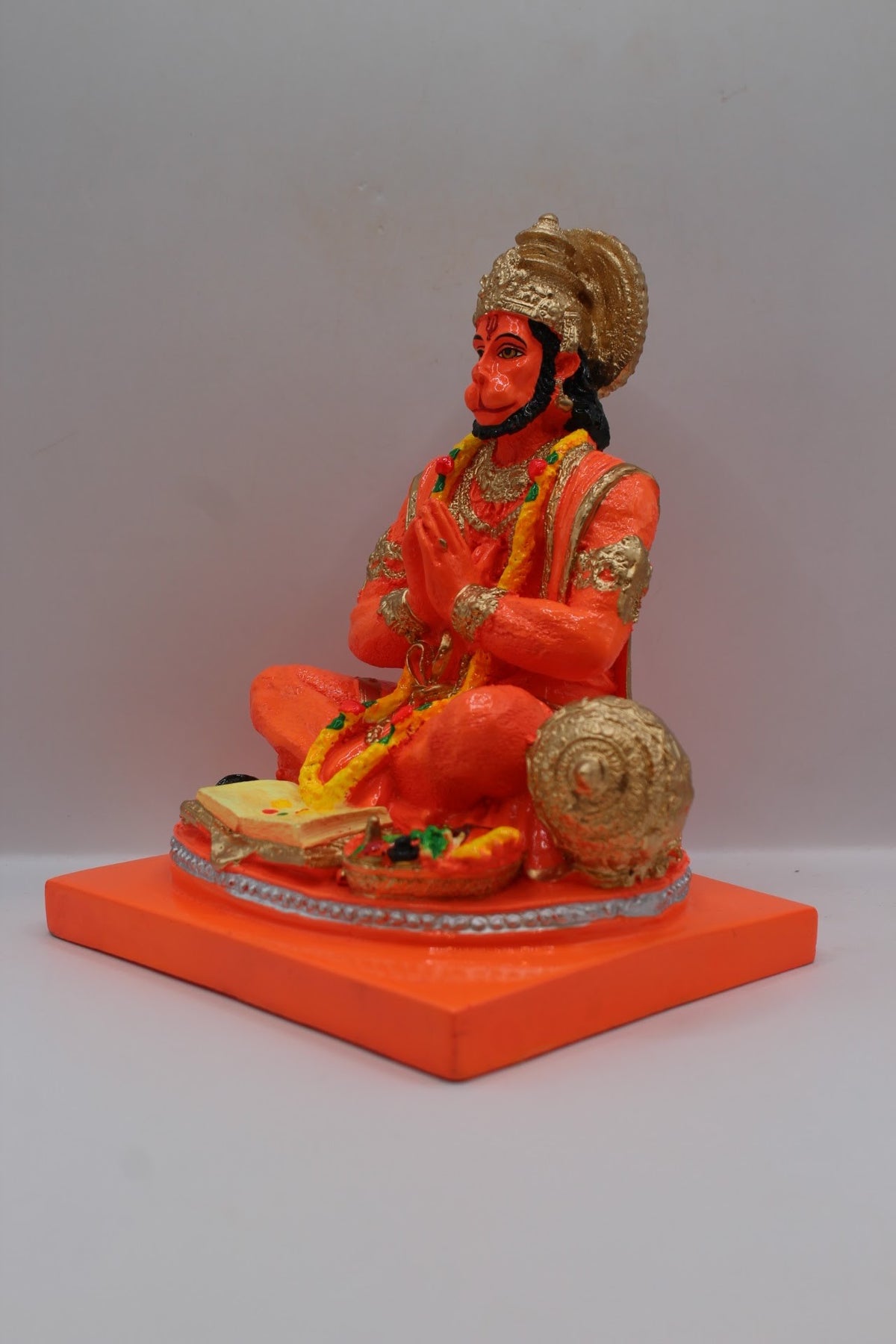 Orange resin Hanuman murti seated in prayer, right side view