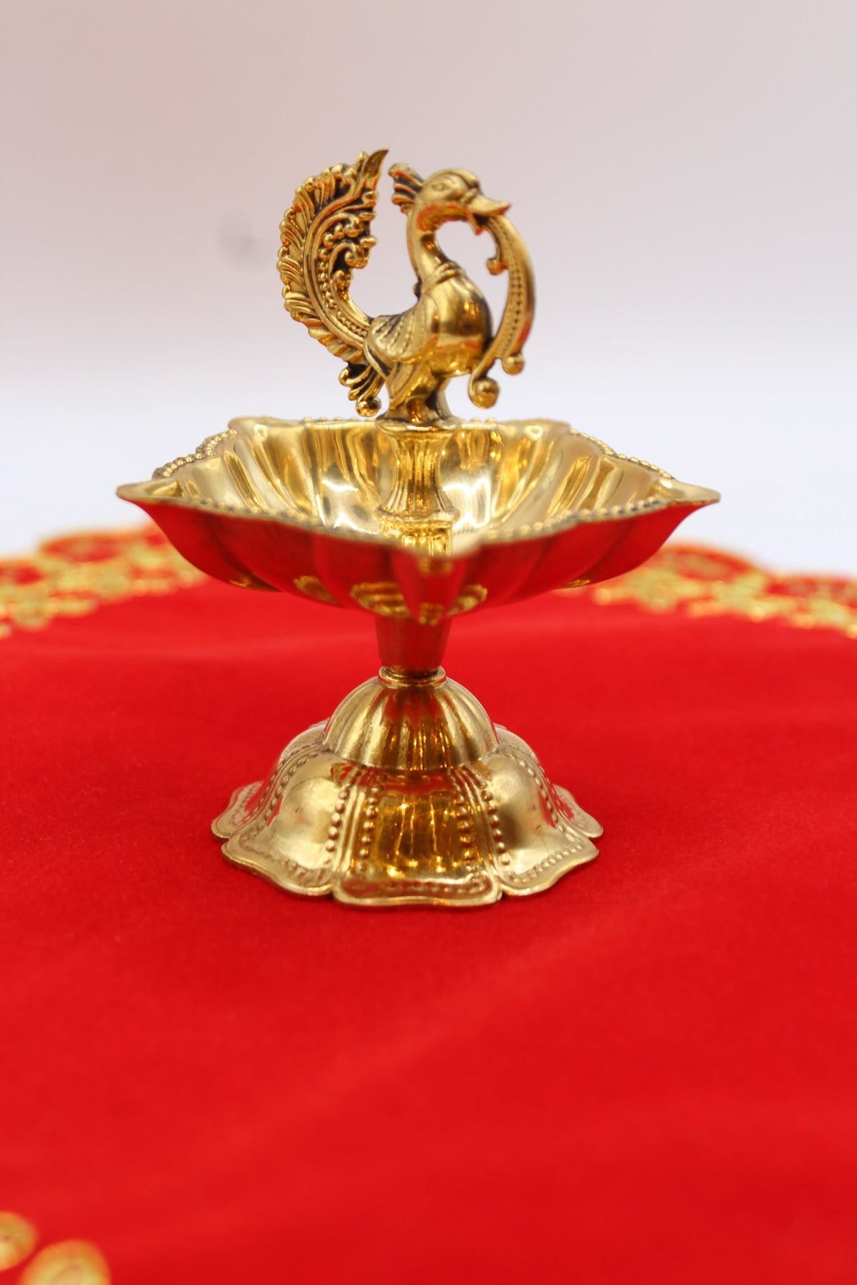 Solid brass peacock diya with a scalloped bowl raised on a fluted pedestal
