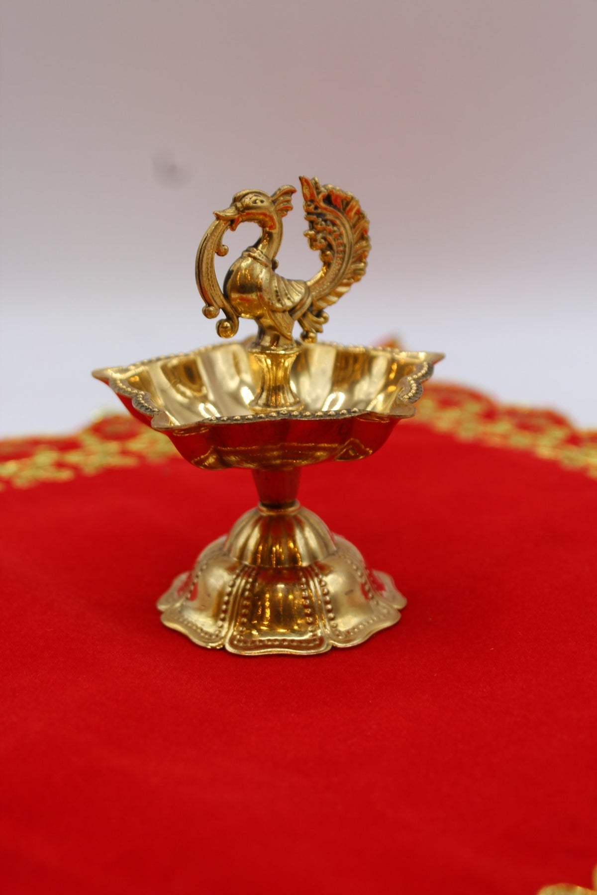 Solid brass peacock diya with a scalloped bowl raised on a fluted pedestal