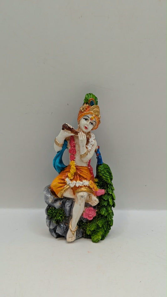 Lord Krishna statue sitting on rock with peacock, front view