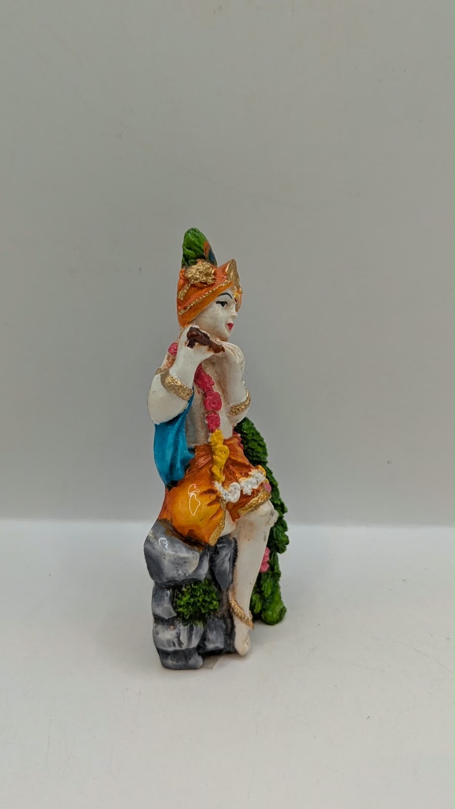 Lord Krishna statue sitting on rock with peacock, side view
