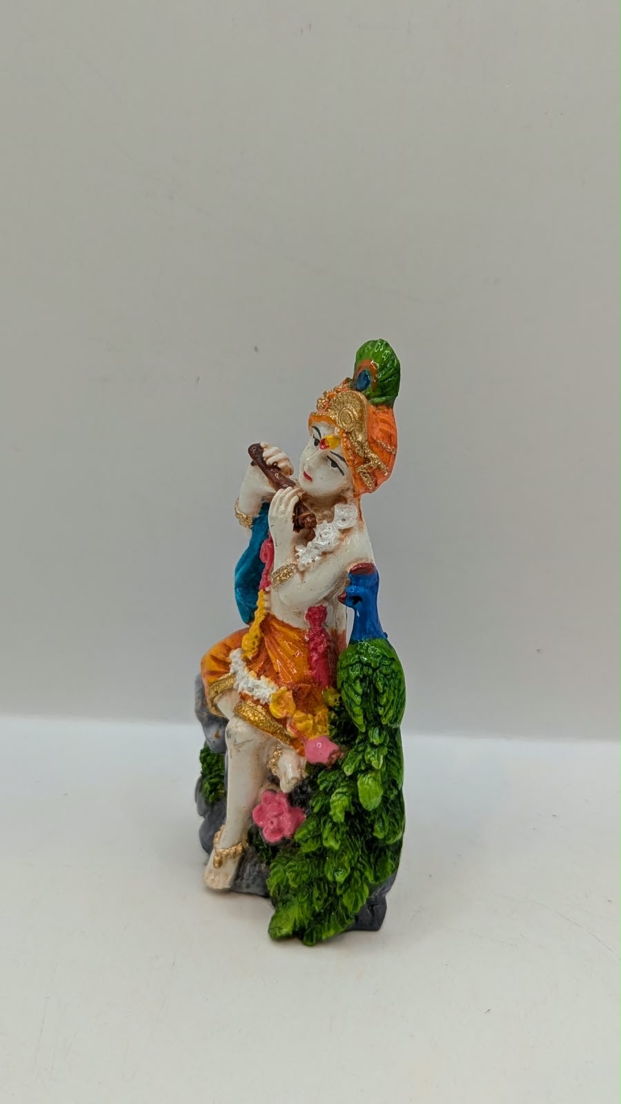 Lord Krishna statue sitting on rock with peacock, other side view
