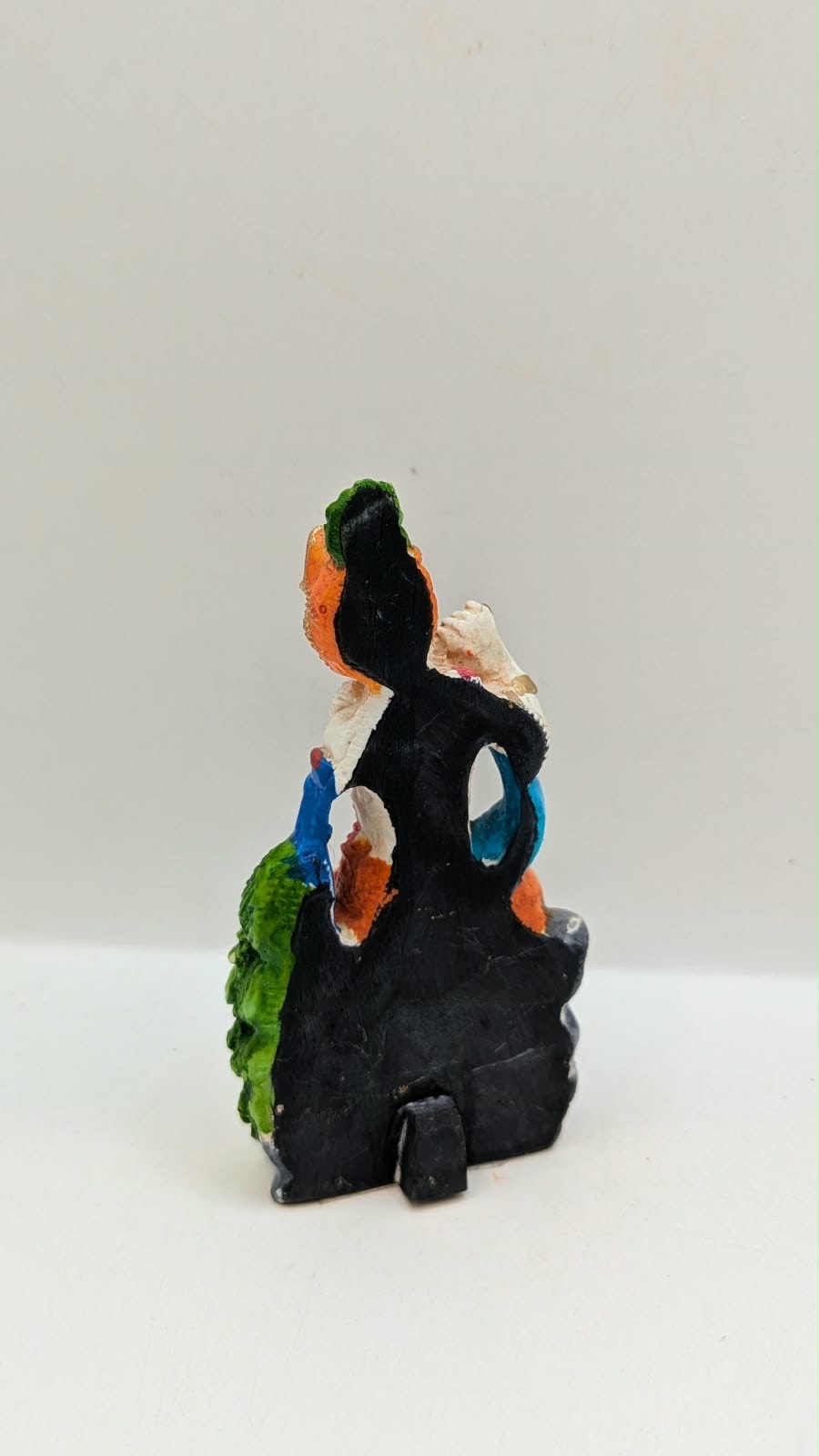 Lord Krishna statue sitting on rock with peacock, back view