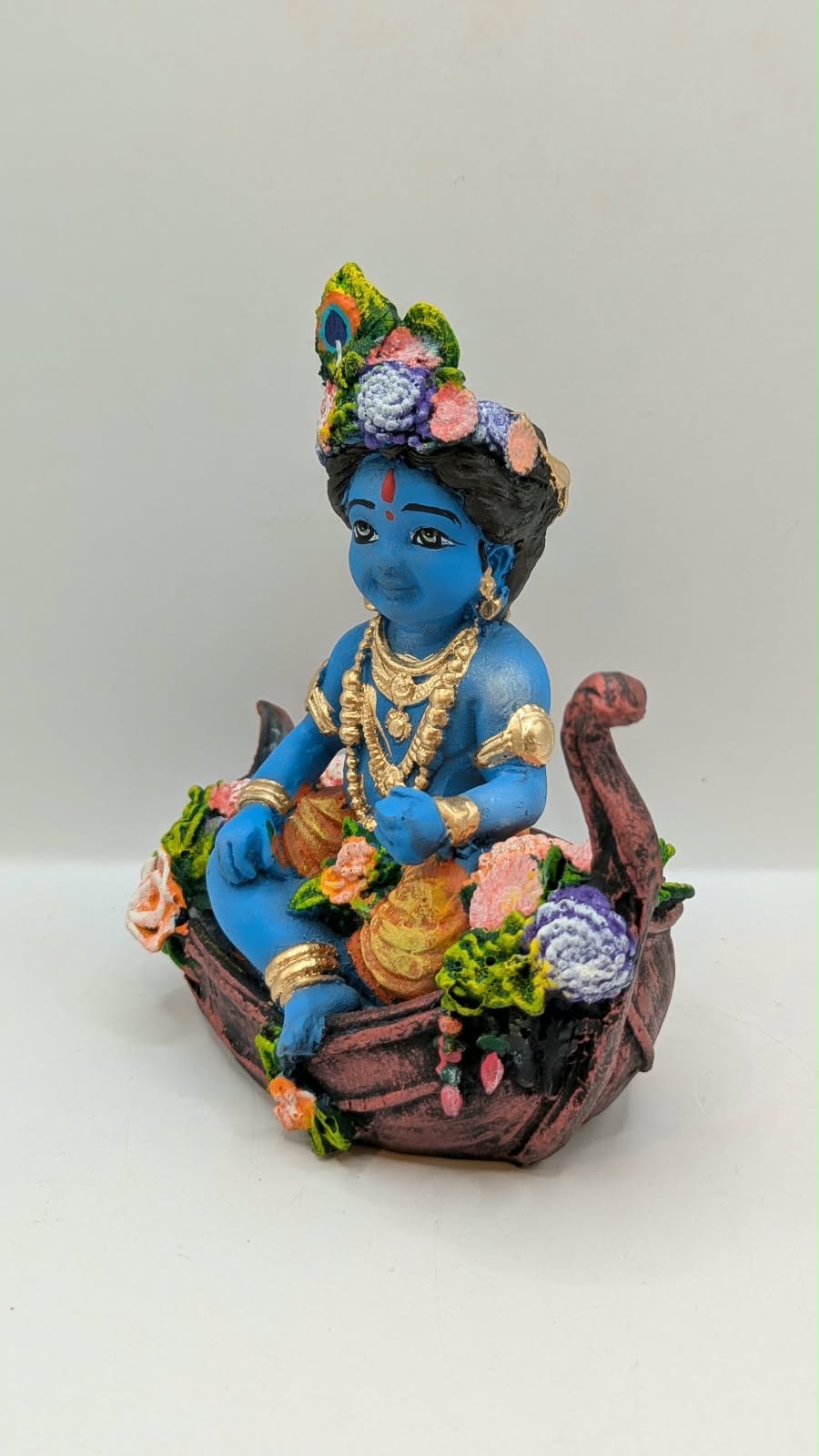 Blue baby Krishna statue on flower boat, other side view