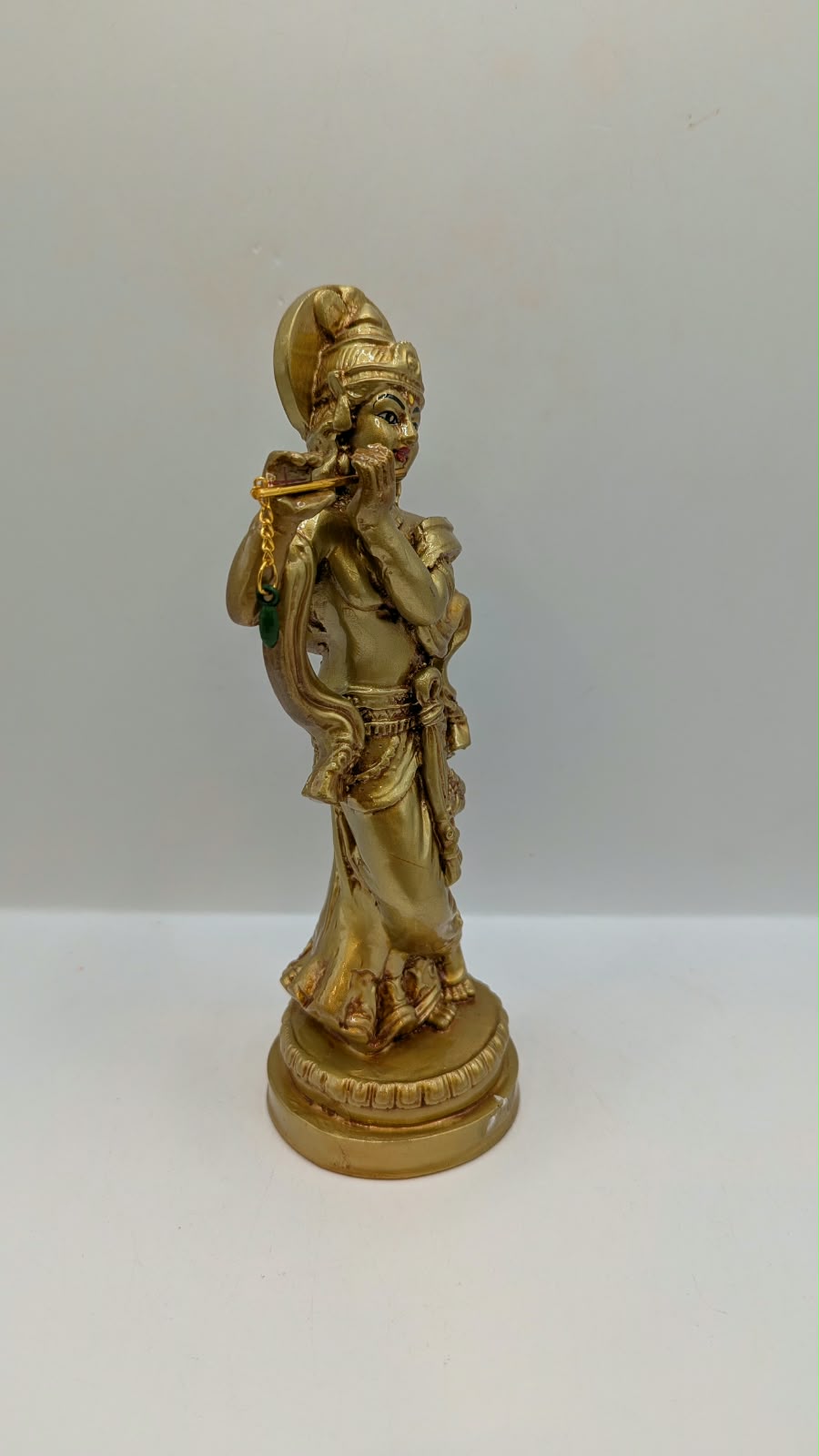 Gold Krishna statue with flute and halo, side view