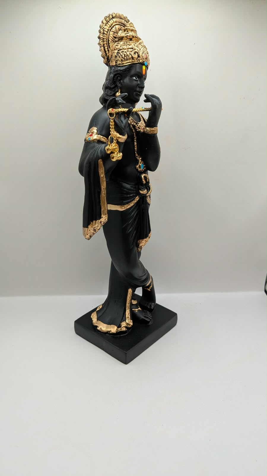 Tall black and gold Krishna statue on square base, side view