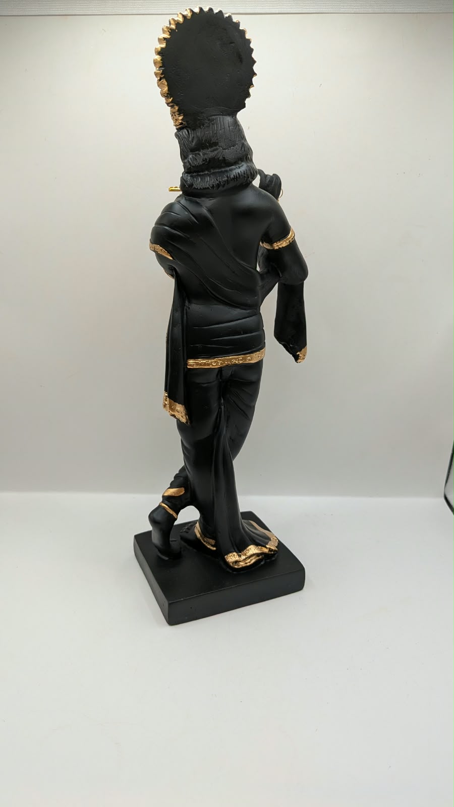 Tall black and gold Krishna statue on square base, back view