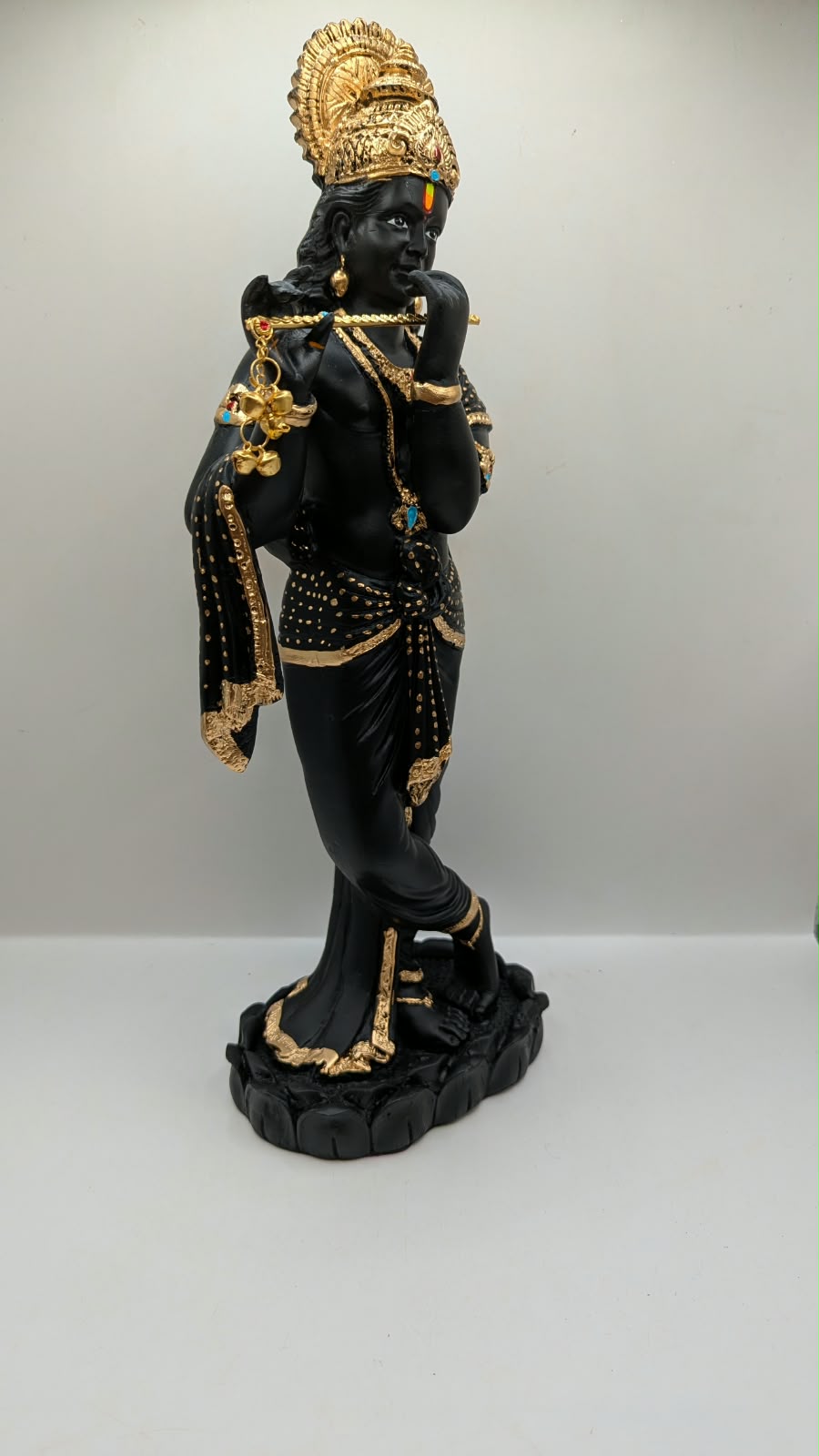 Tall black and gold Krishna statue on lotus base, side view