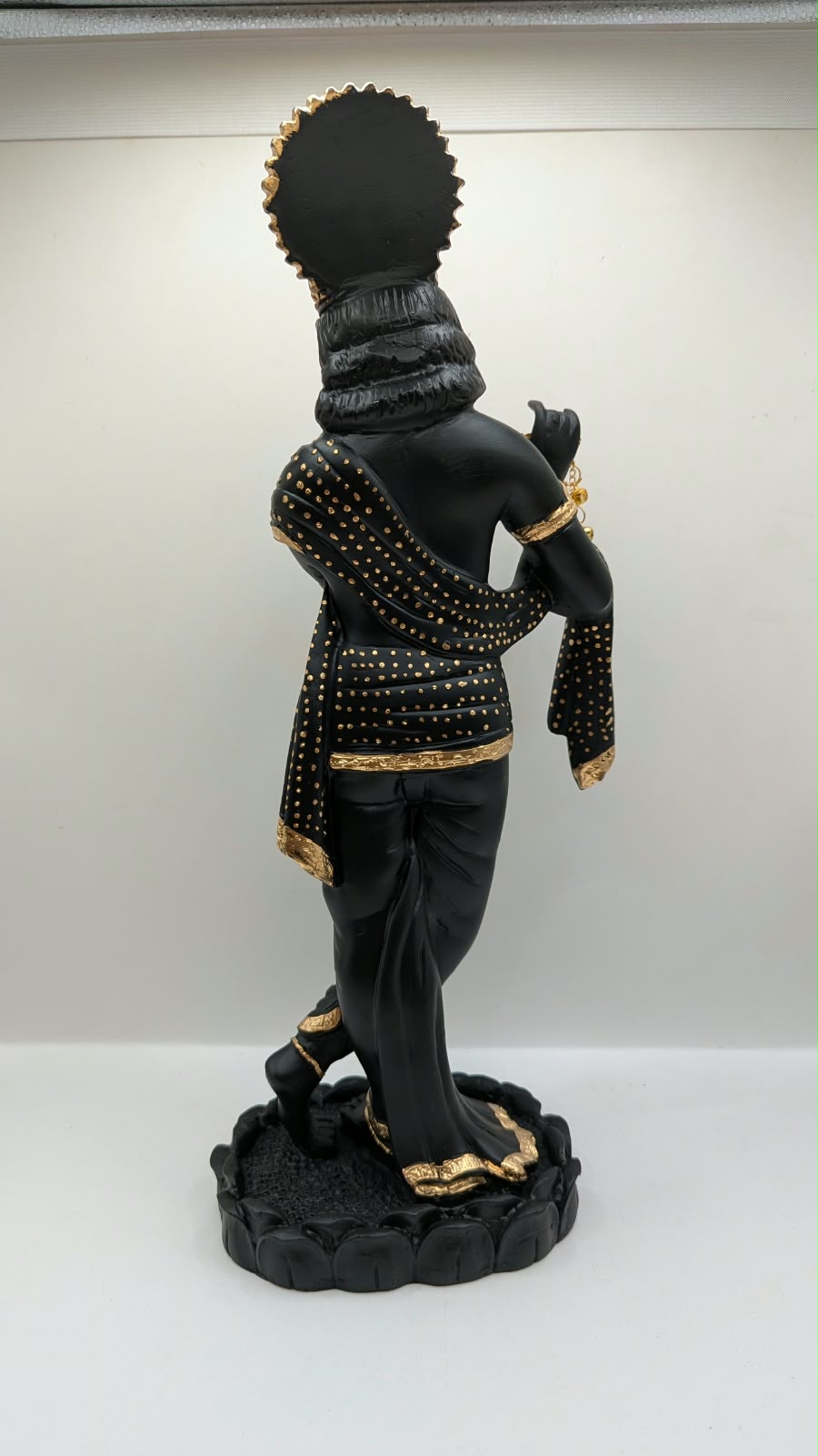 Tall black and gold Krishna statue on lotus base, back view