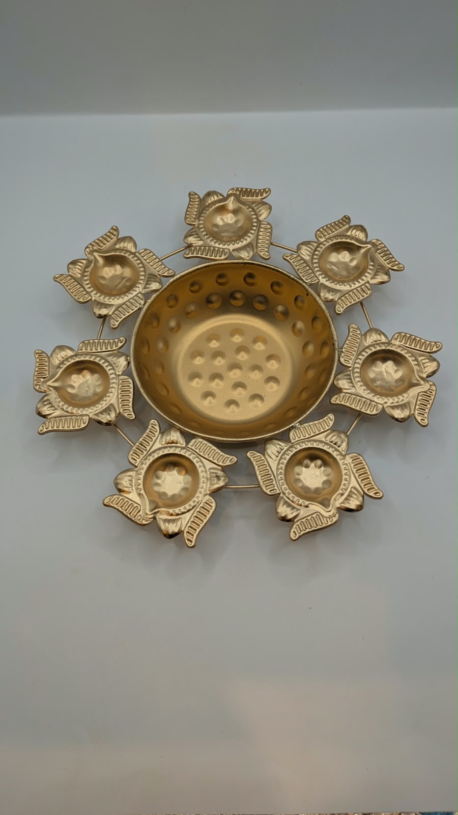 Gold metal urli bowl with 7 lotus diyas, top view