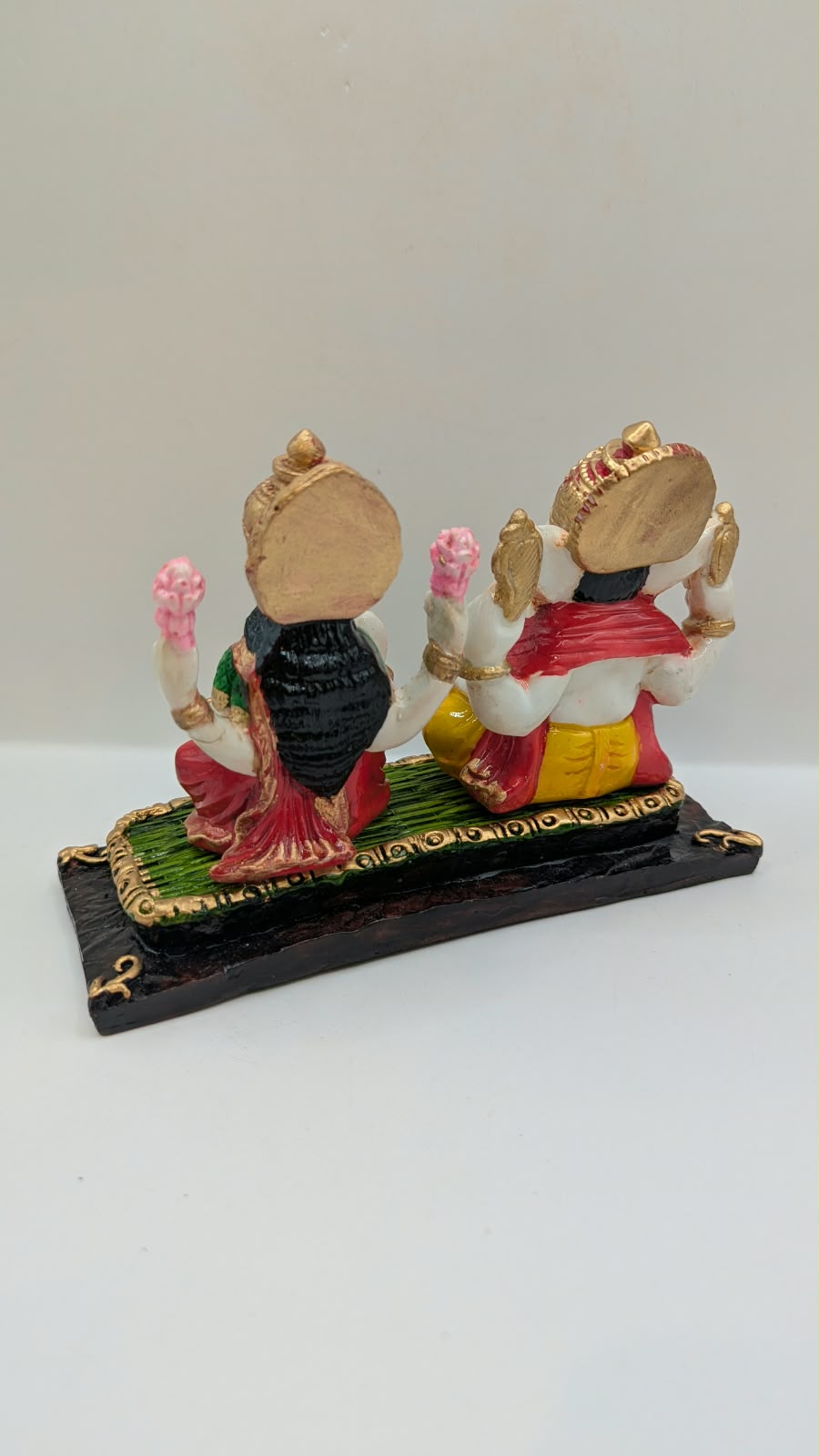 Ganesh and Laxmi statue on green mat, back view