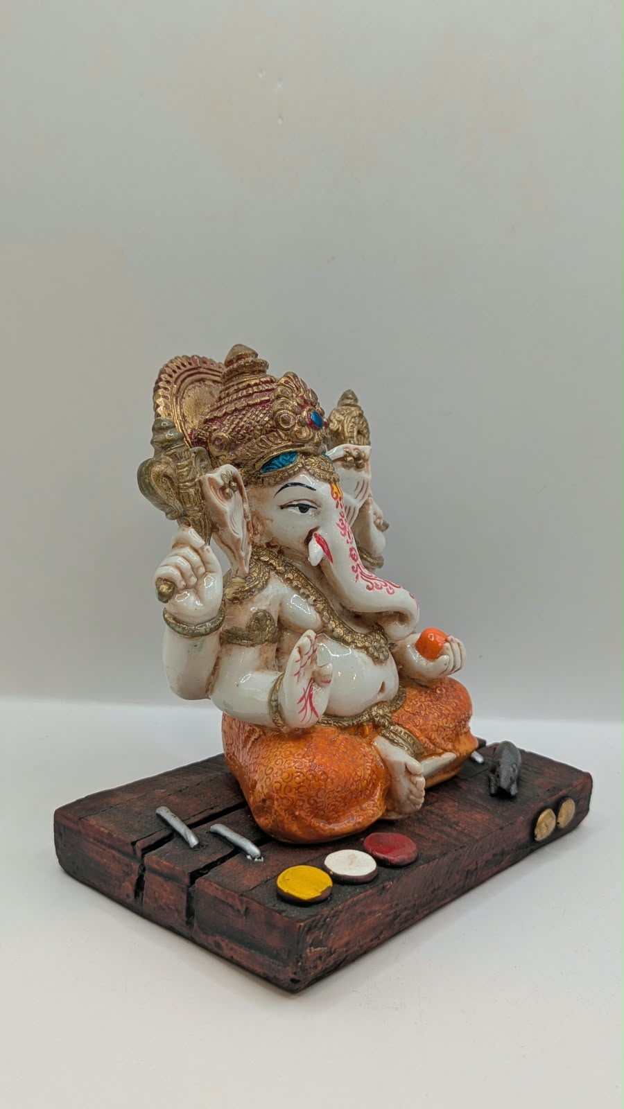 White and orange Ganesh resin statue on wood-look base, side view