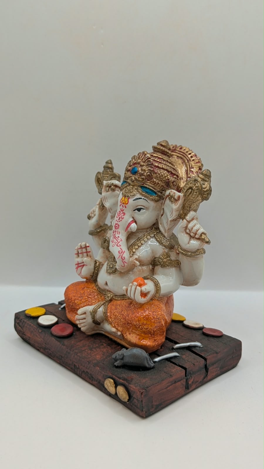 White and orange Ganesh resin statue on wood-look base, other side view