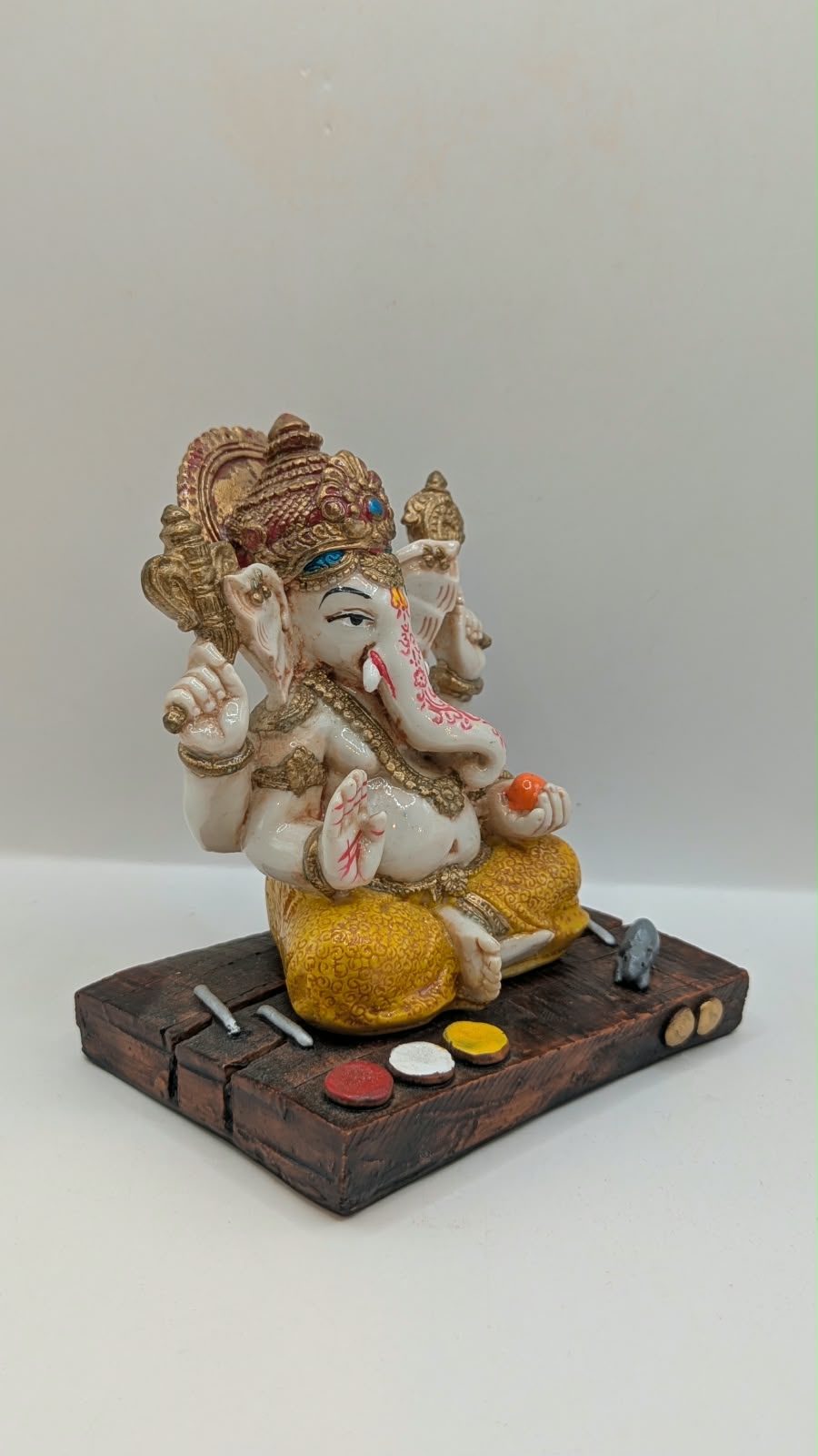 White and yellow Ganesh resin statue on wood-look base, side view