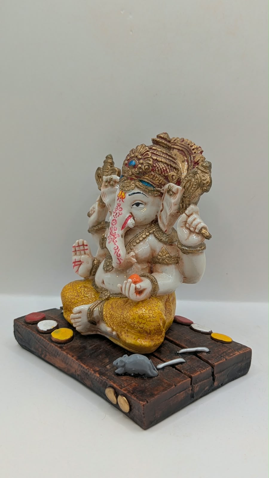 White and yellow Ganesh resin statue on wood-look base, other side view