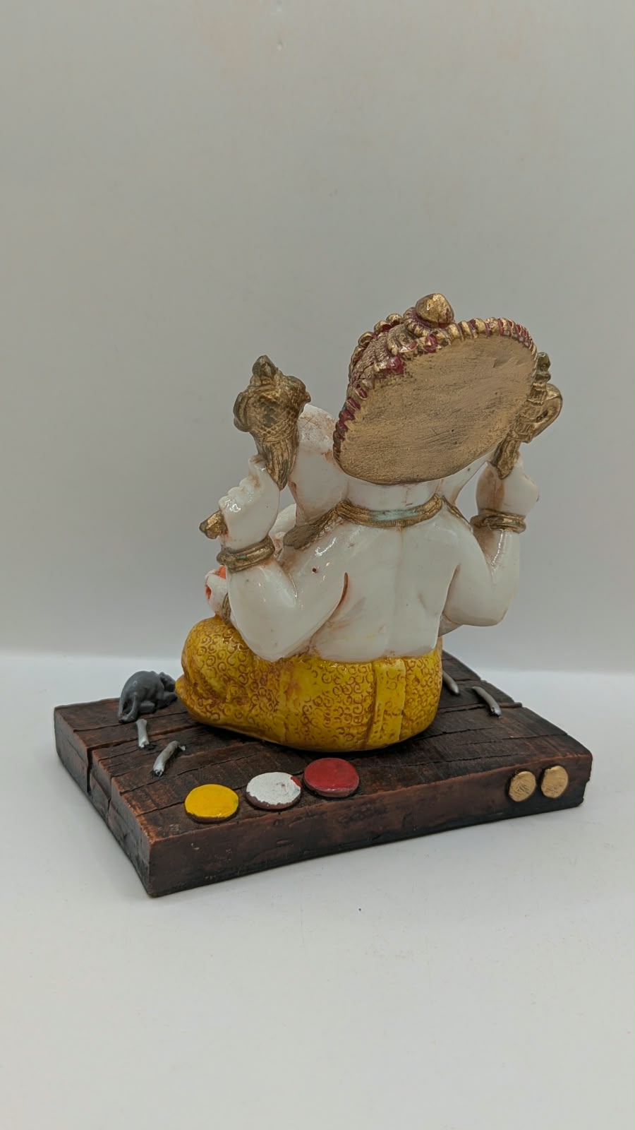 White and yellow Ganesh resin statue on wood-look base, back view