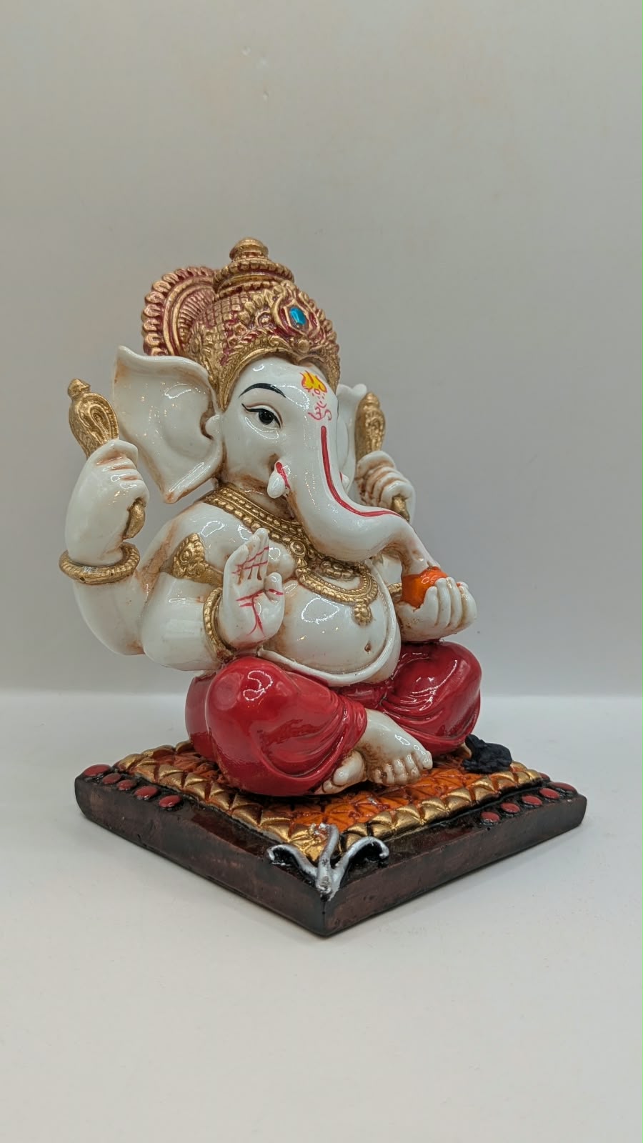 White and red Ganesh resin statue with copper crown, side view
