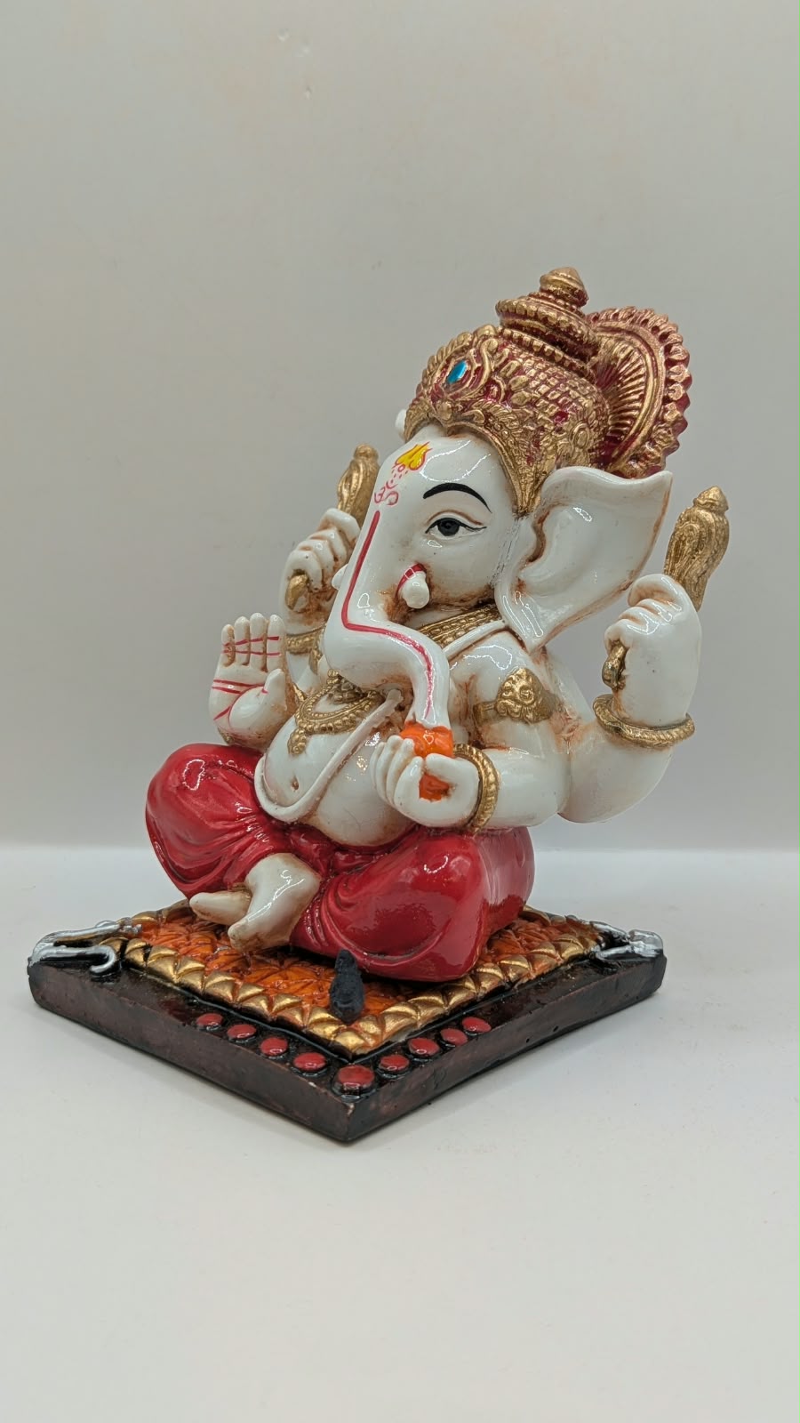 White and red Ganesh resin statue with copper crown, other side view