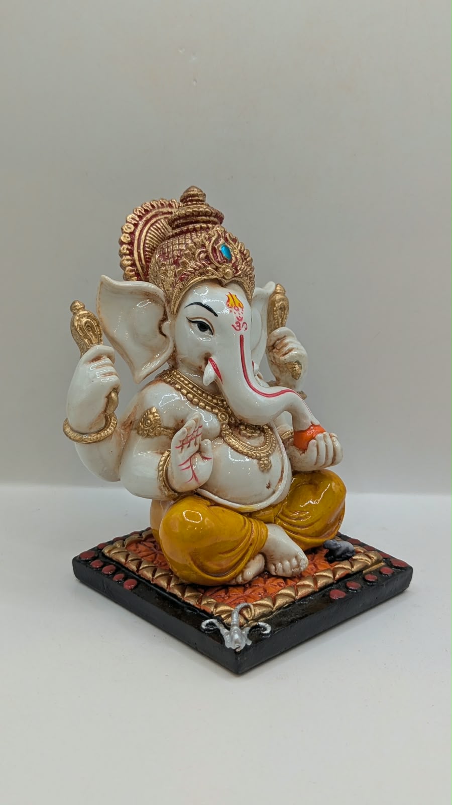 White and yellow Ganesh resin statue with copper crown, side view