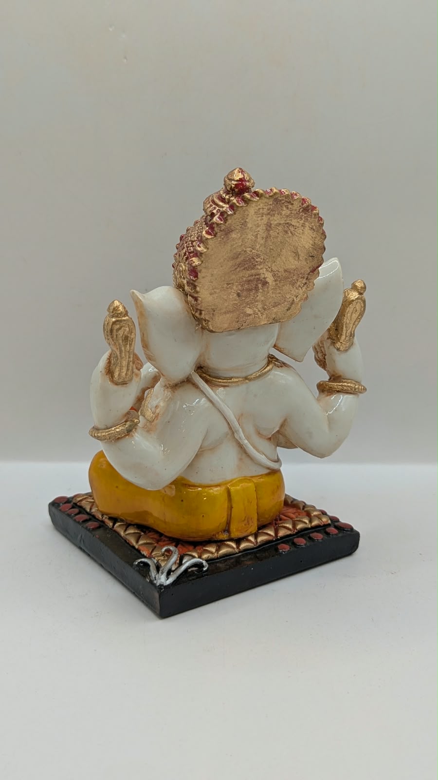 White and yellow Ganesh resin statue with copper crown, back view
