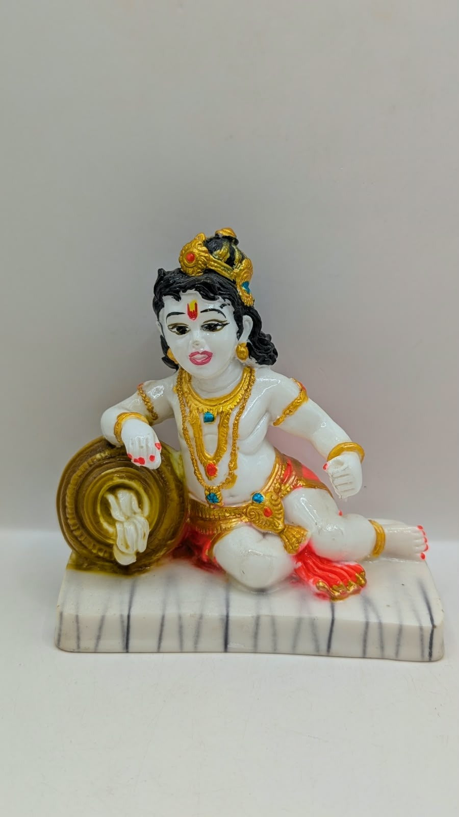 White baby Krishna statue with gold pot and red dhoti, front view
