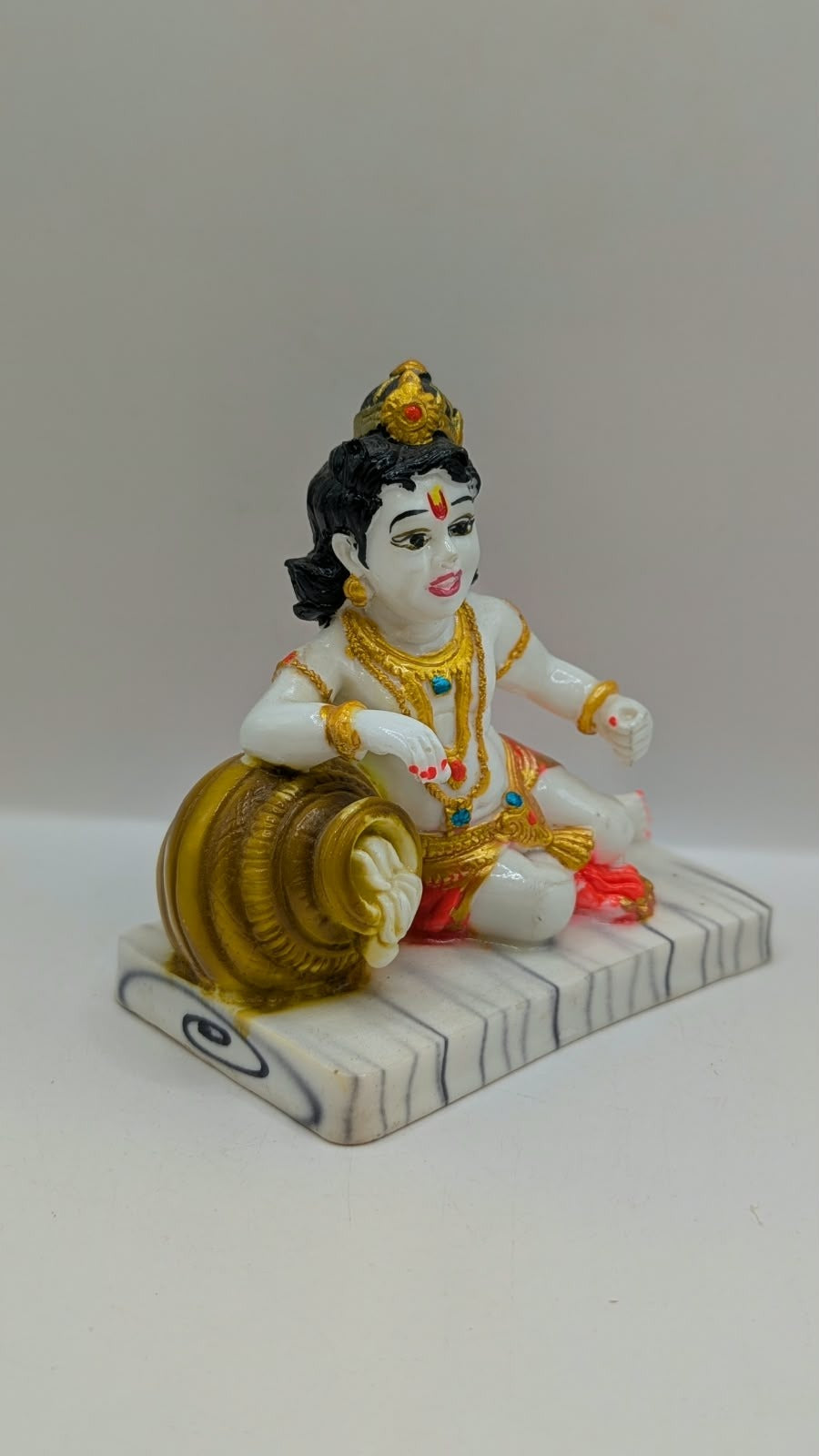 White baby Krishna statue with gold pot and red dhoti, side view