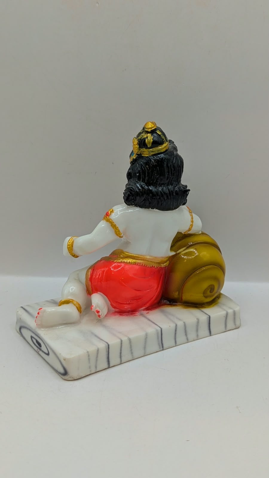 White baby Krishna statue with gold pot and red dhoti, back view