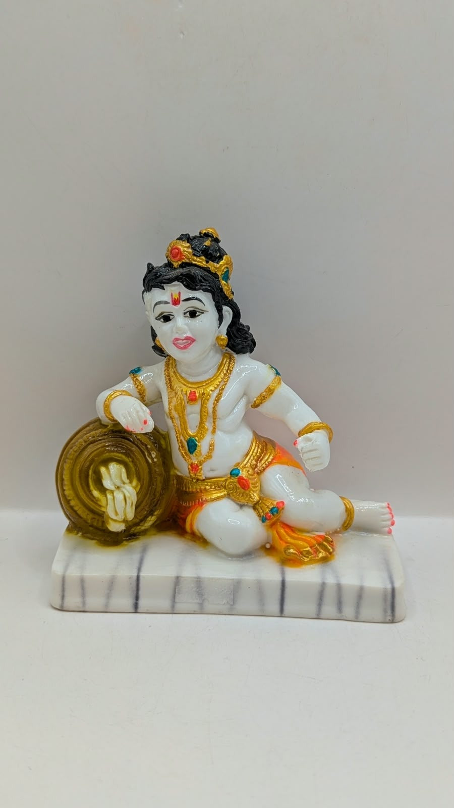 White baby Krishna statue with gold pot and orange dhoti, front view