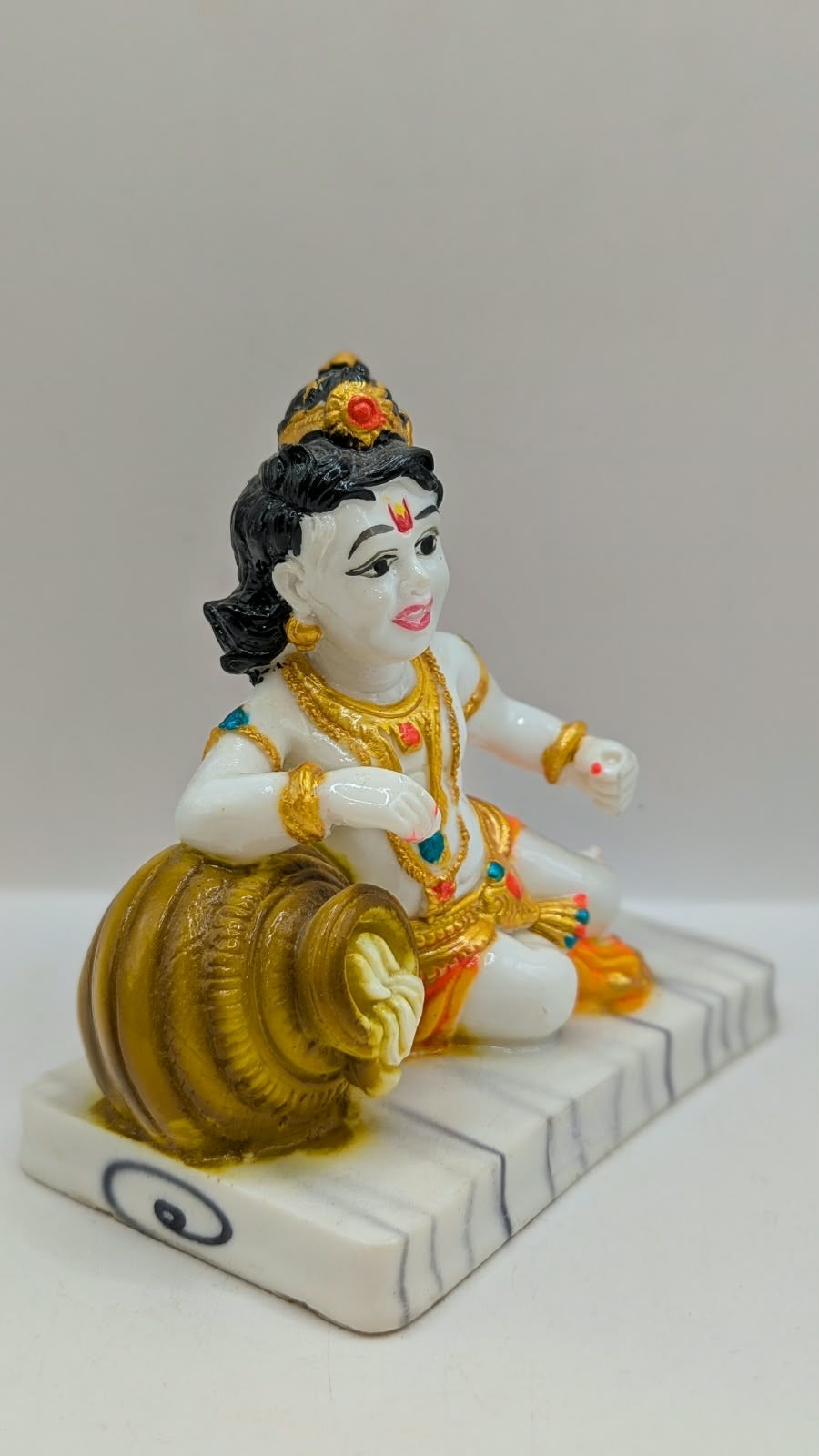 White baby Krishna statue with gold pot and orange dhoti, side view