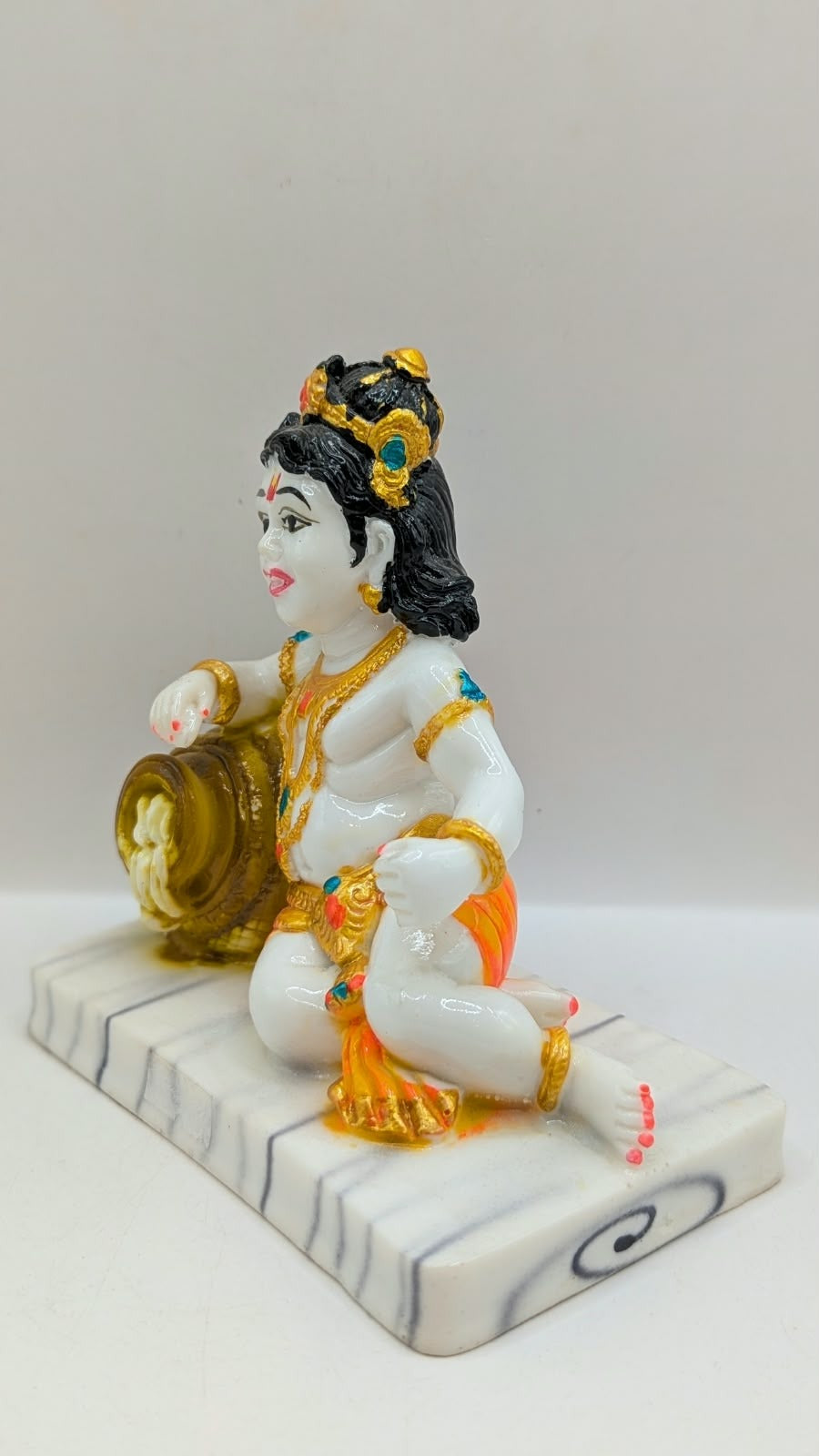 White baby Krishna statue with gold pot and orange dhoti, other side view