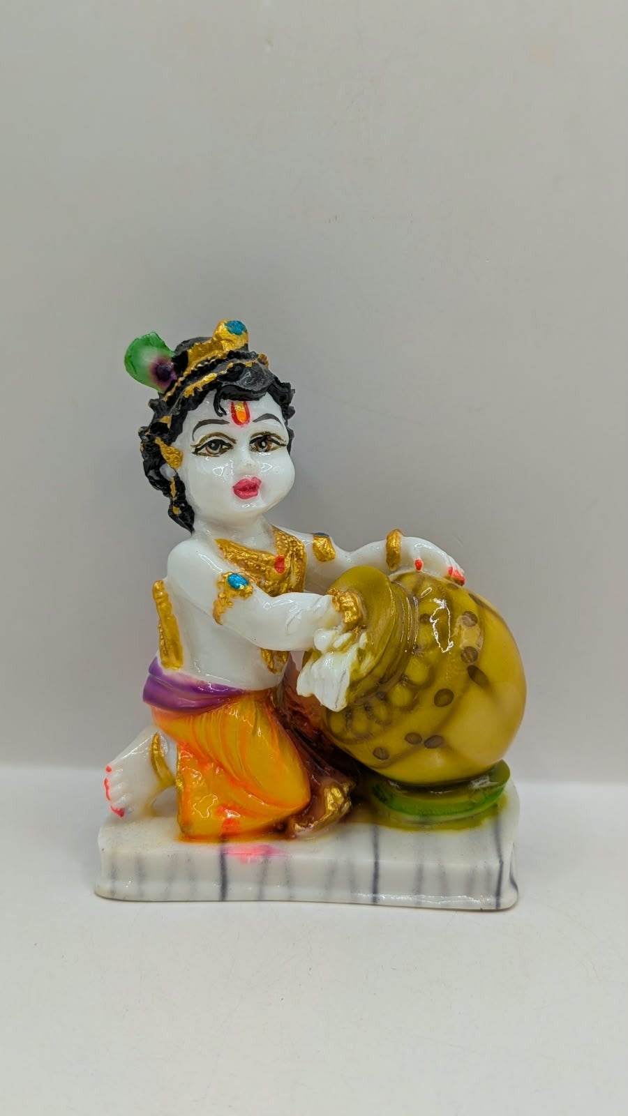 White baby Krishna statue hugging gold butter pot, front view