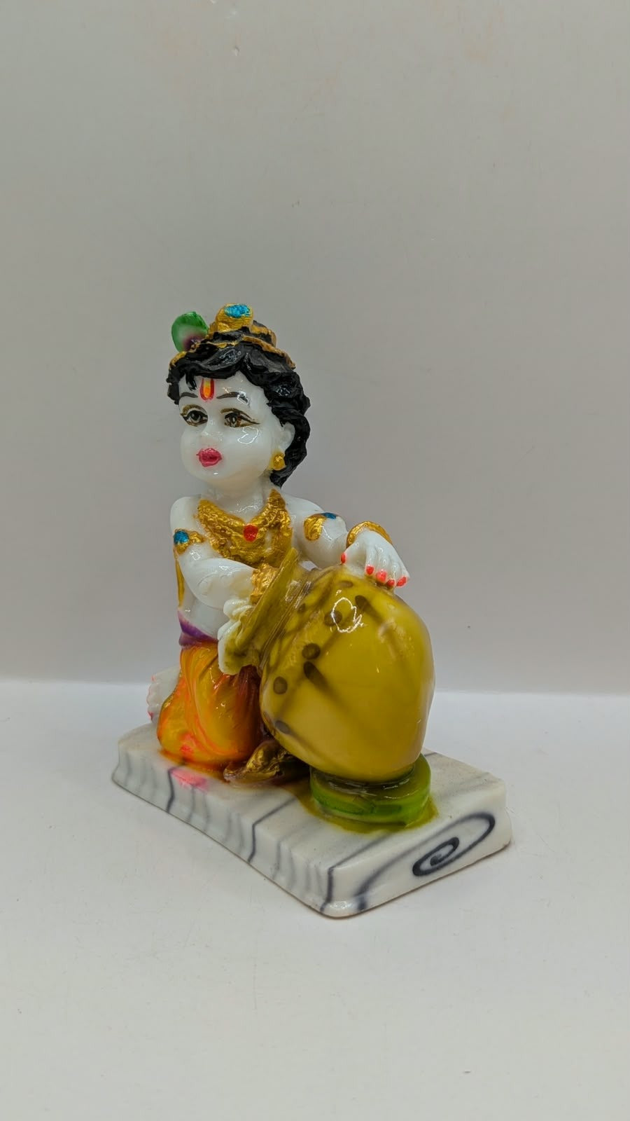 White baby Krishna statue hugging gold butter pot, other side view