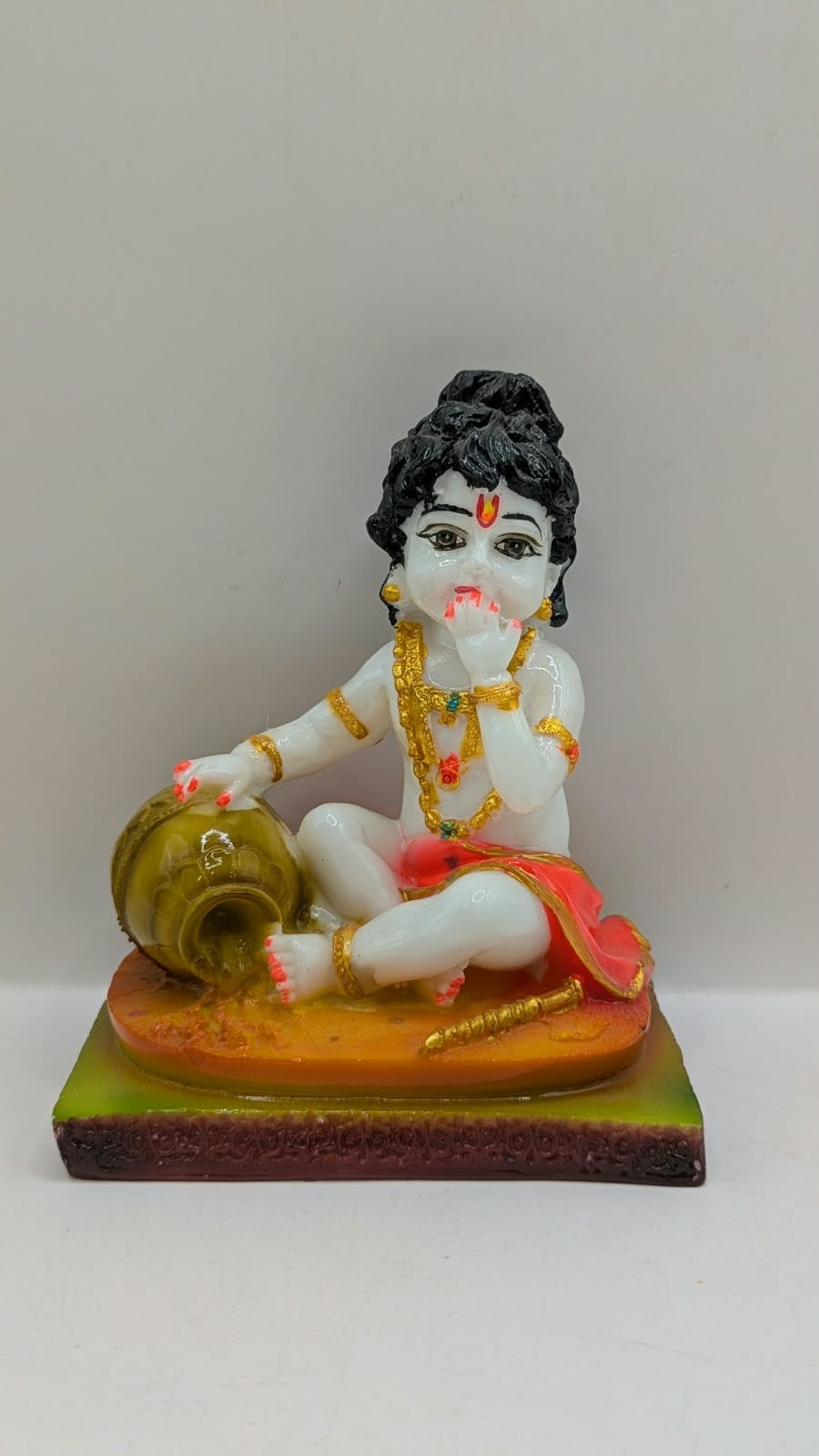 White baby Krishna statue eating butter, orange base, front view