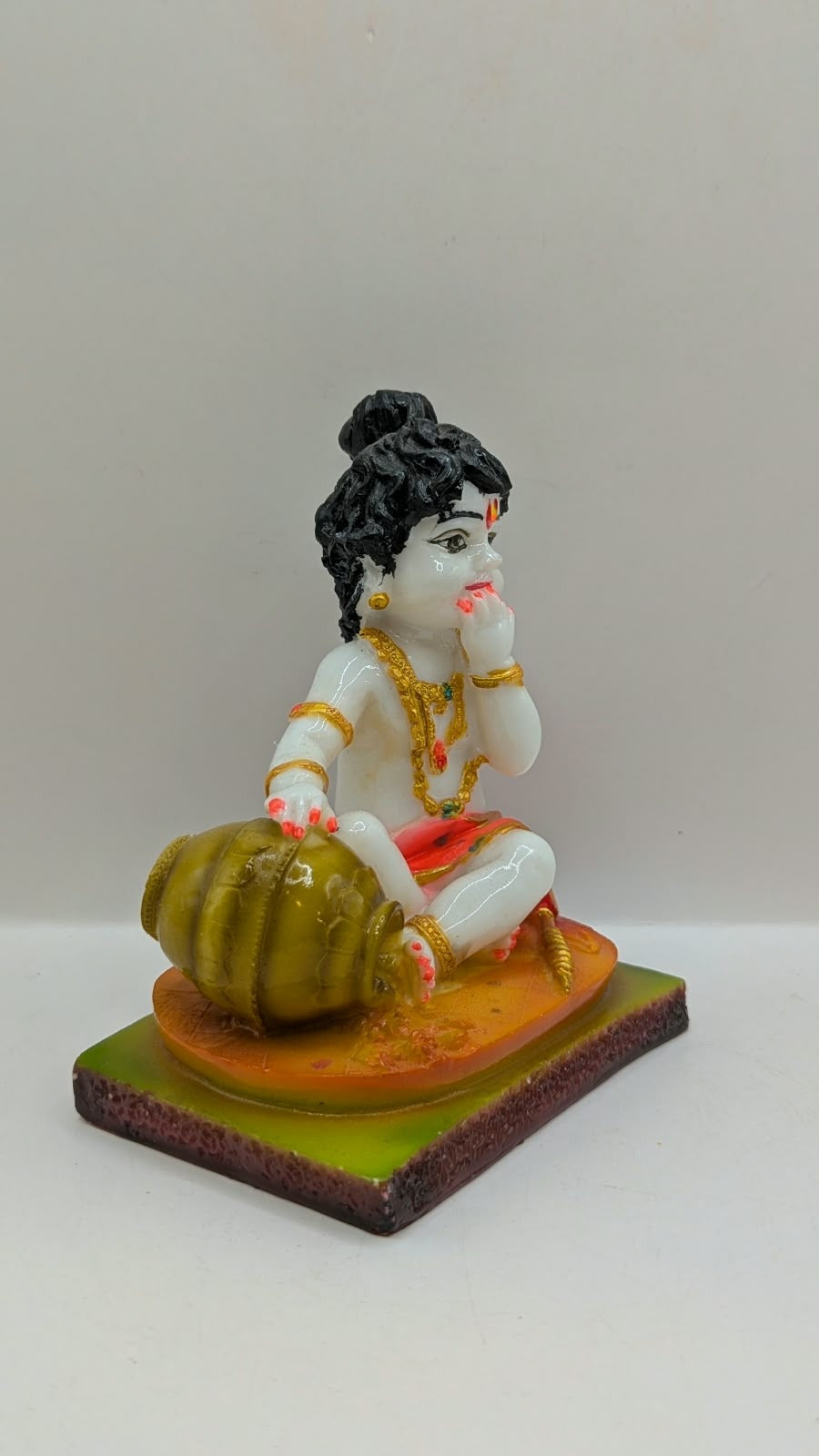 White baby Krishna statue eating butter, orange base, side view
