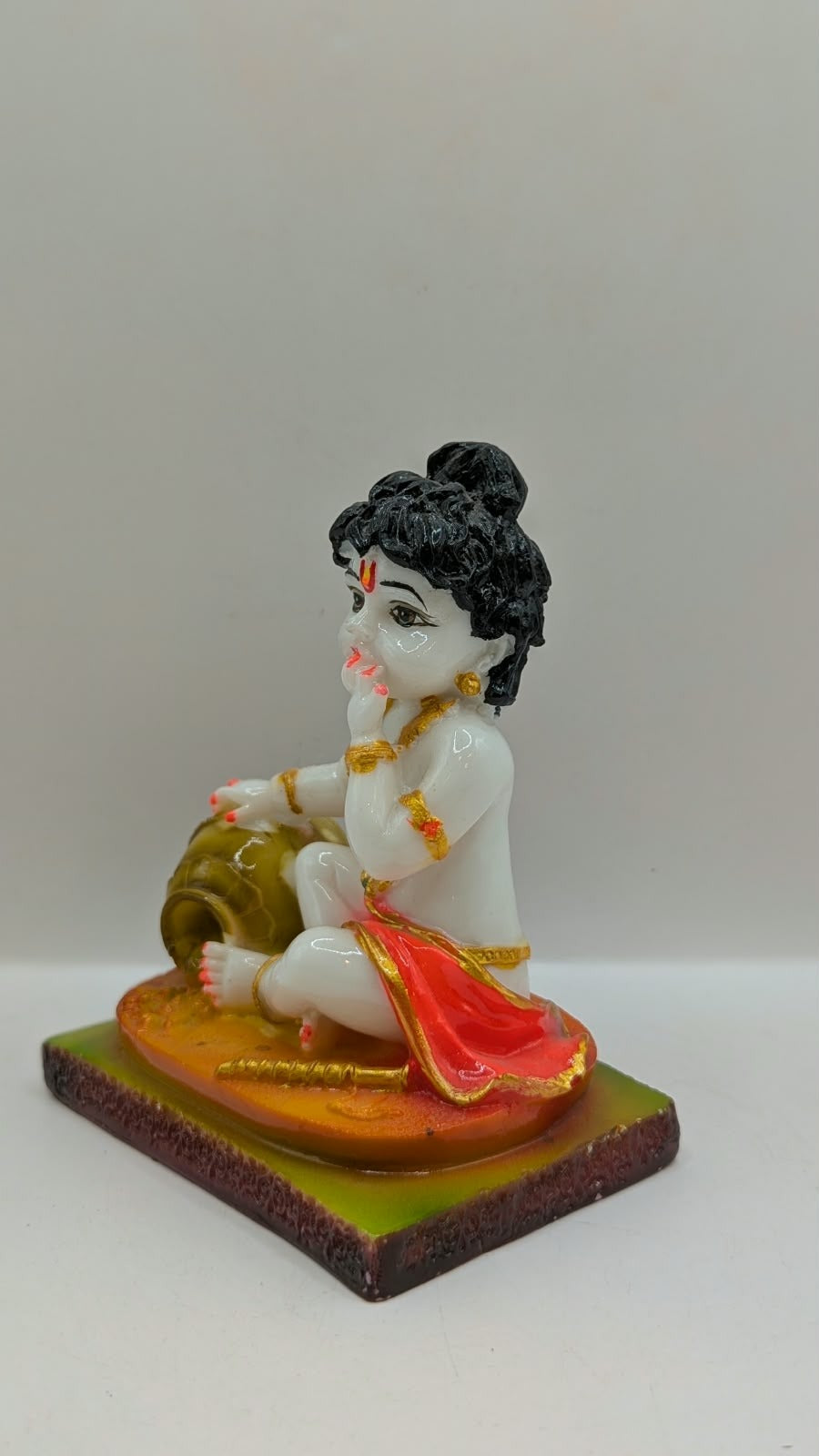 White baby Krishna statue eating butter, orange base, other side view