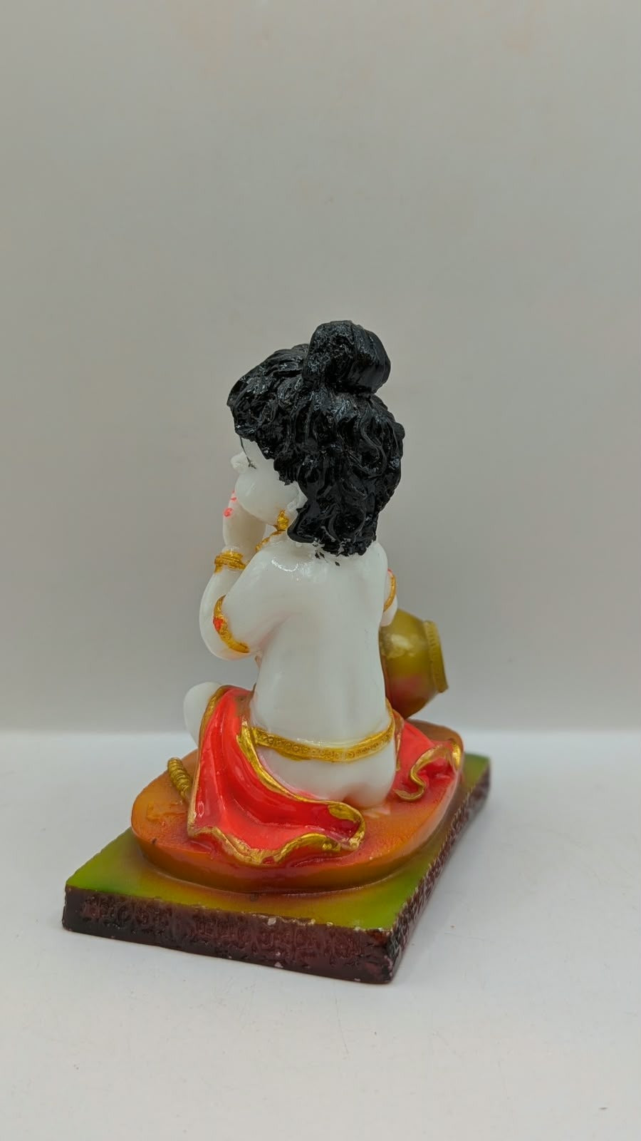 White baby Krishna statue eating butter, orange base, back view