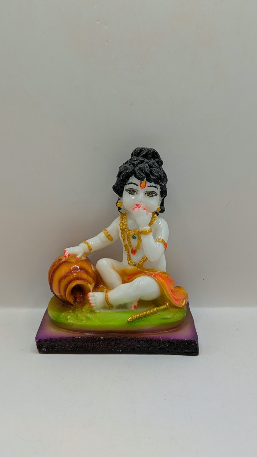 White baby Krishna statue eating butter, green base, front view