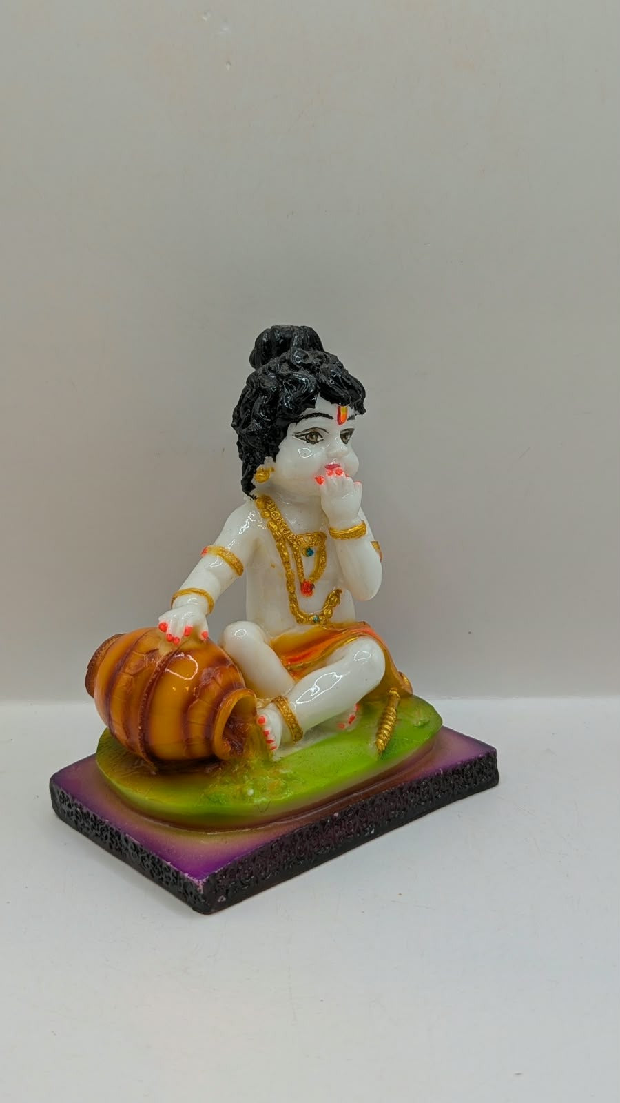 White baby Krishna statue eating butter, green base, side view