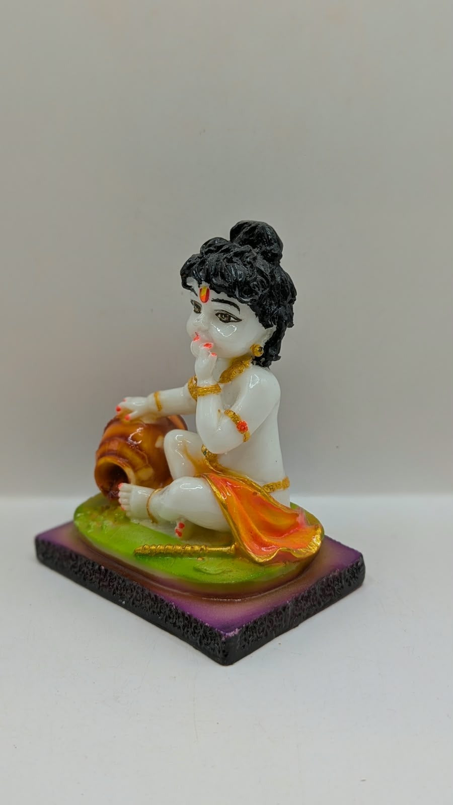 White baby Krishna statue eating butter, green base, other side view